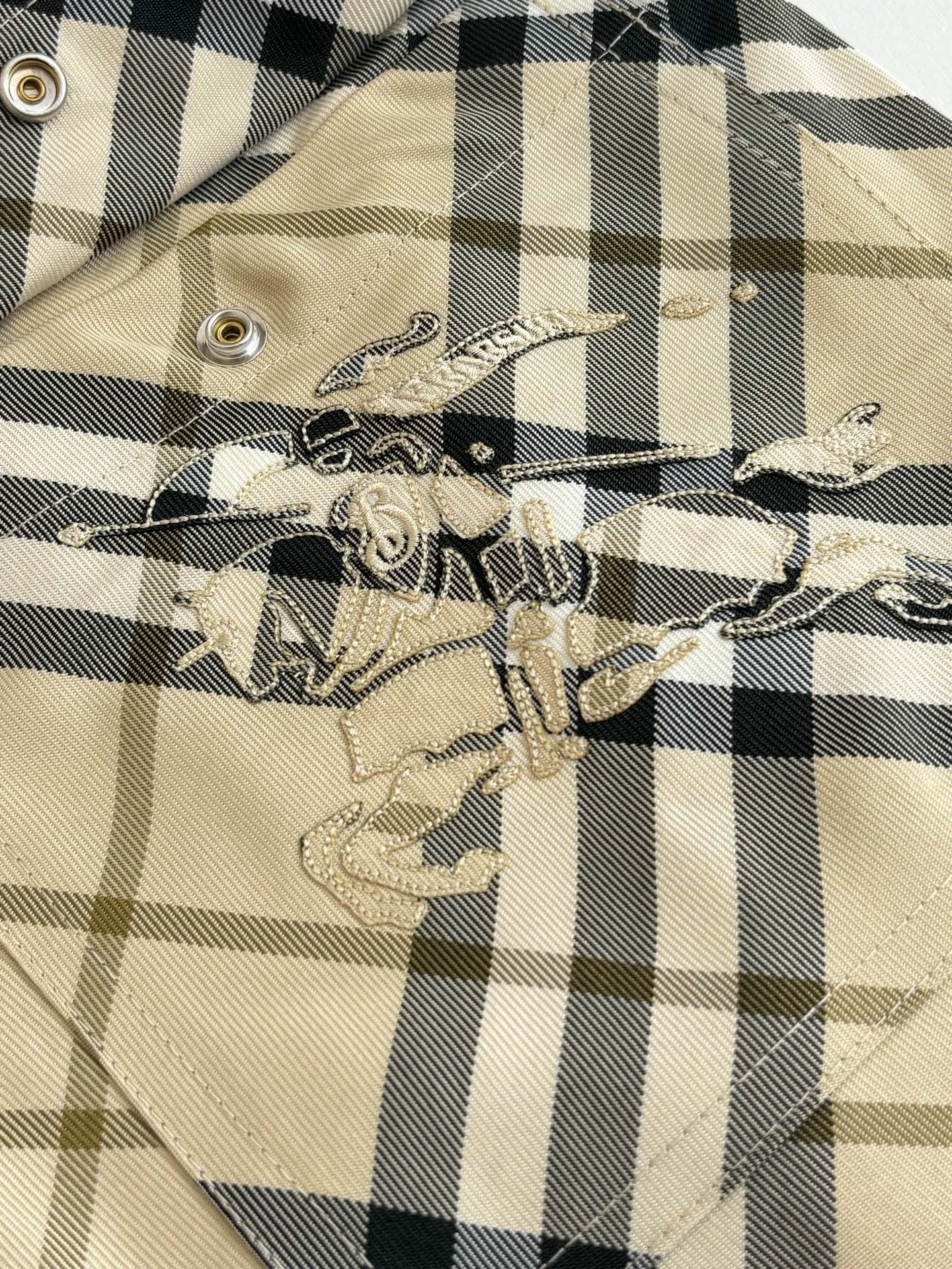 Burberry plaid shorts embroidery patch detail on beige and black check fabric.