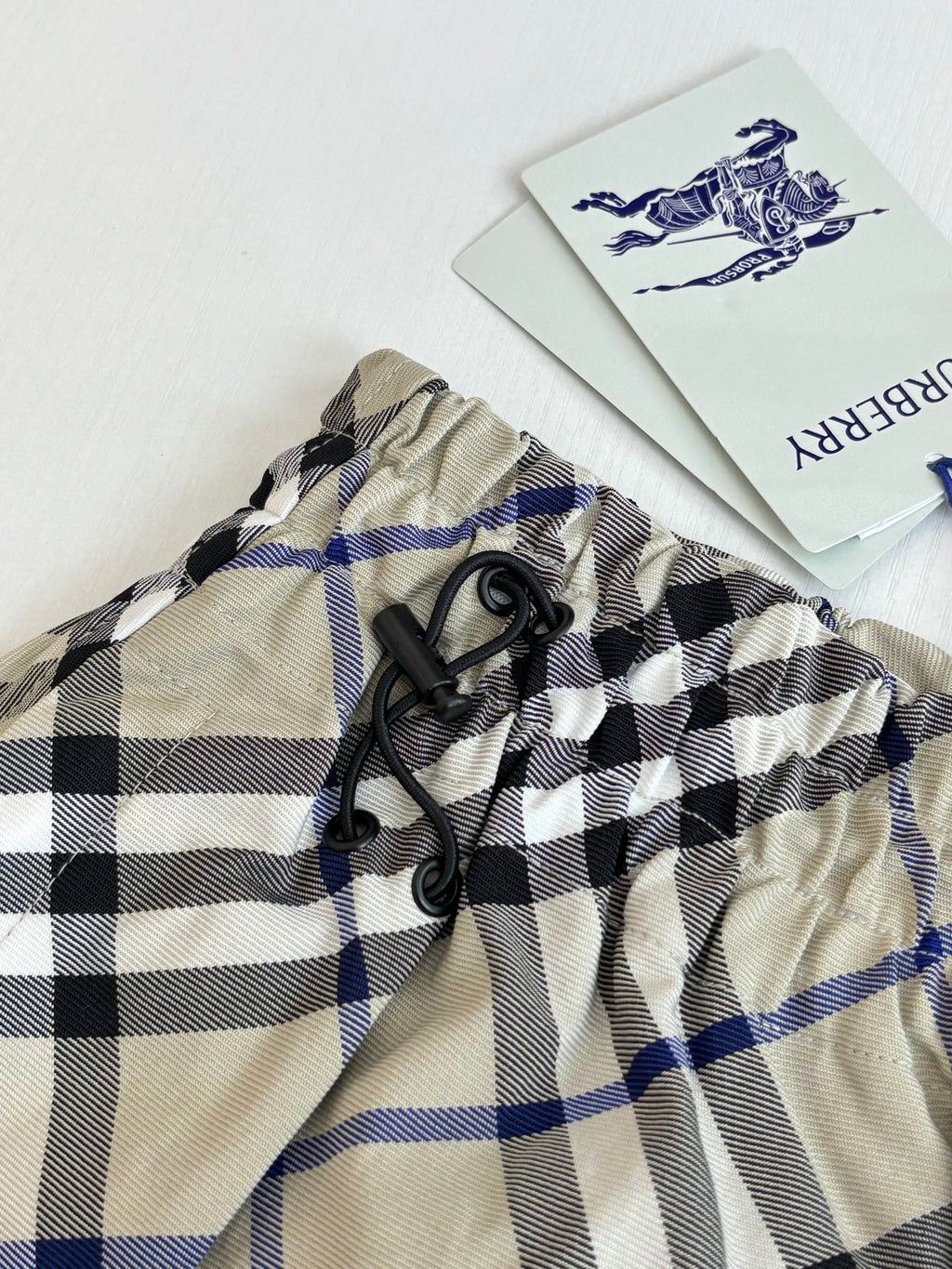 Plaid waistband close-up with black drawstring ties and brand label, beige blue and black checks