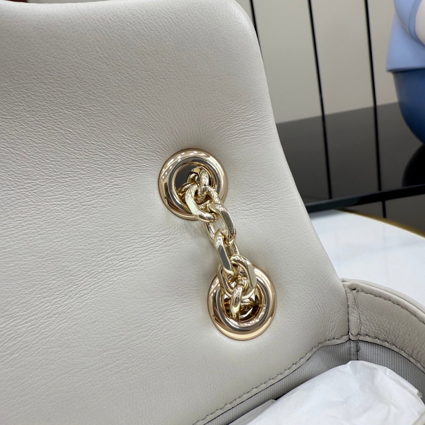 Off-white leather bag corner with gold-tone chain loop hardware and stitched trim