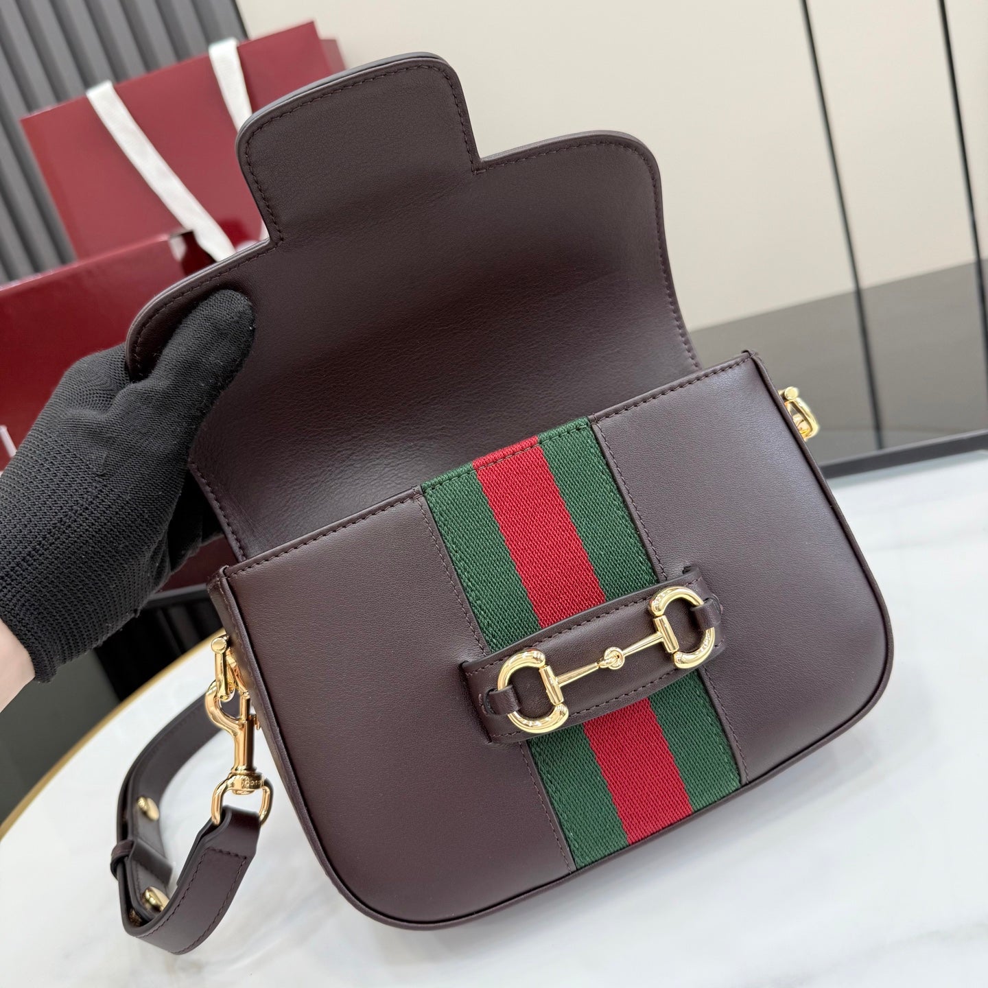 Dark brown leather small flap bag with green and red stripe, gold buckle and strap