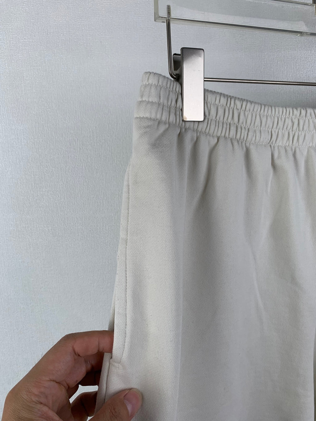 White shorts with elastic waistband, held up at the side seam by a hand