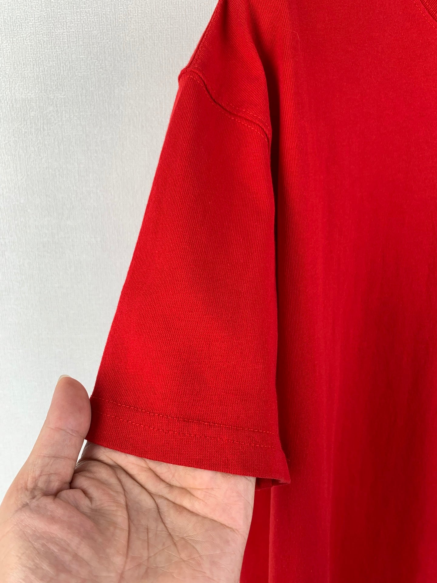 Red short-sleeve T-shirt sleeve detail, hand holding shoulder seam.