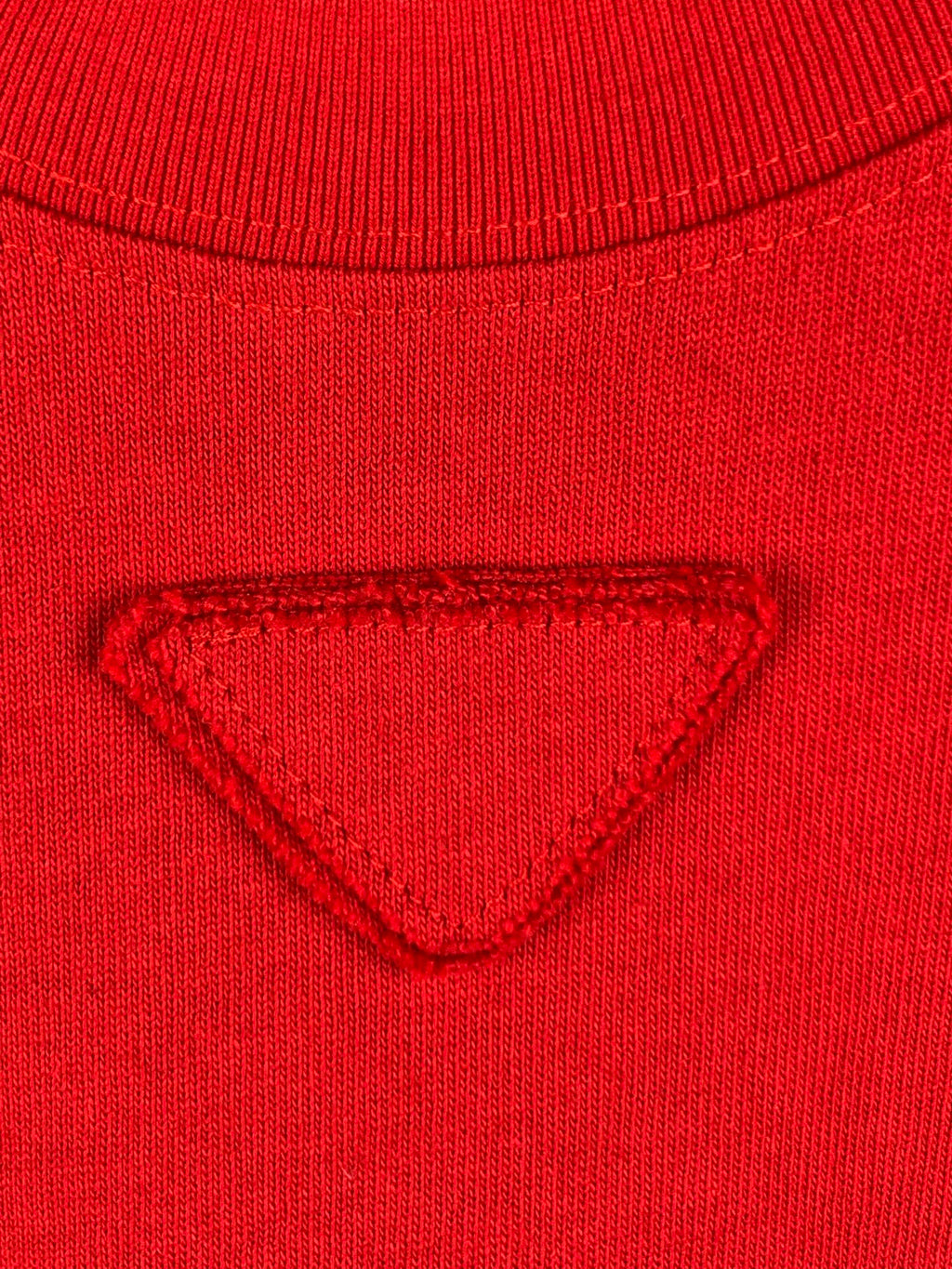 Red knit T-shirt chest with triangular embossed/embroidered emblem.