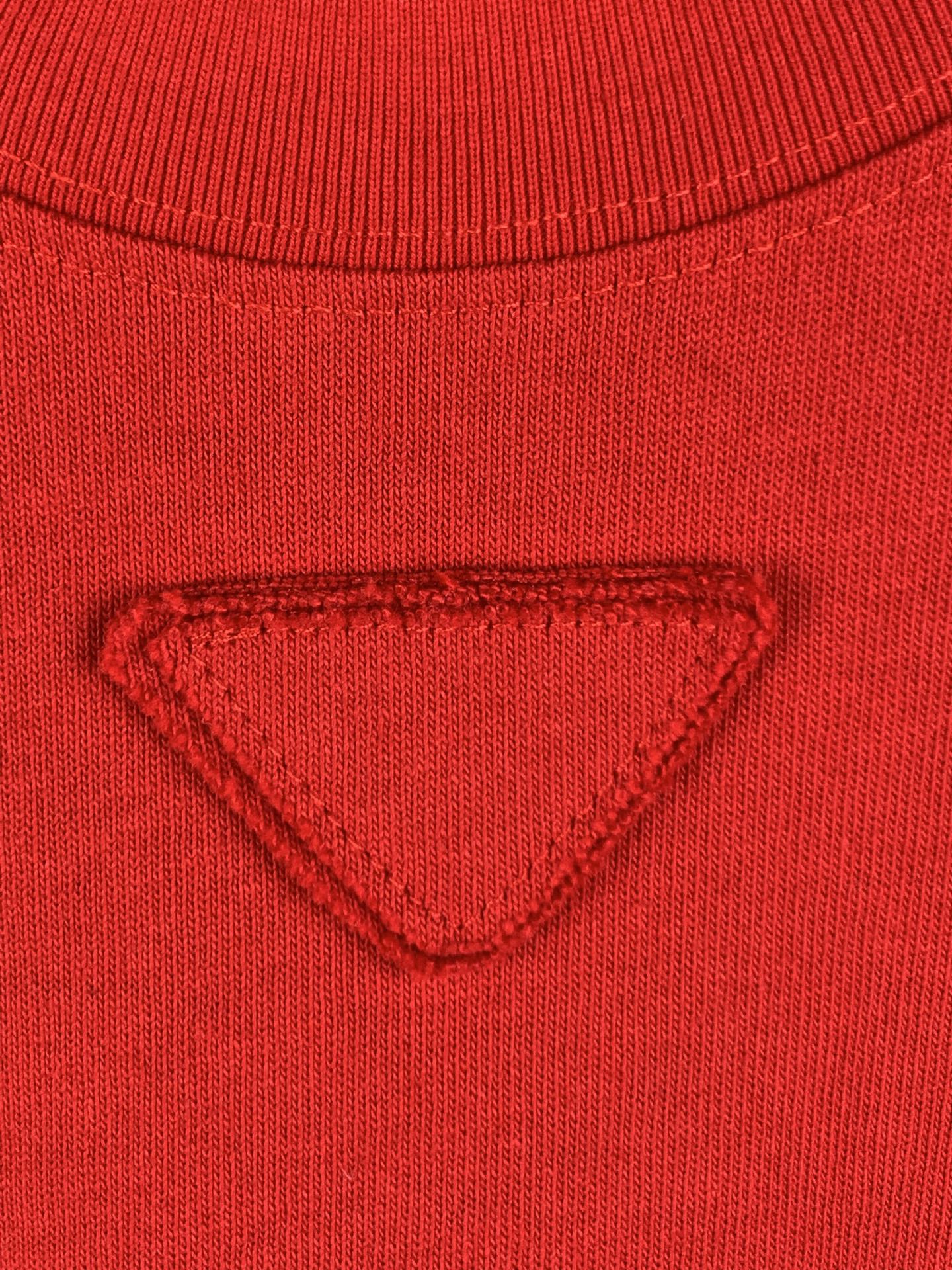 Red knit T-shirt chest with triangular embossed/embroidered emblem.