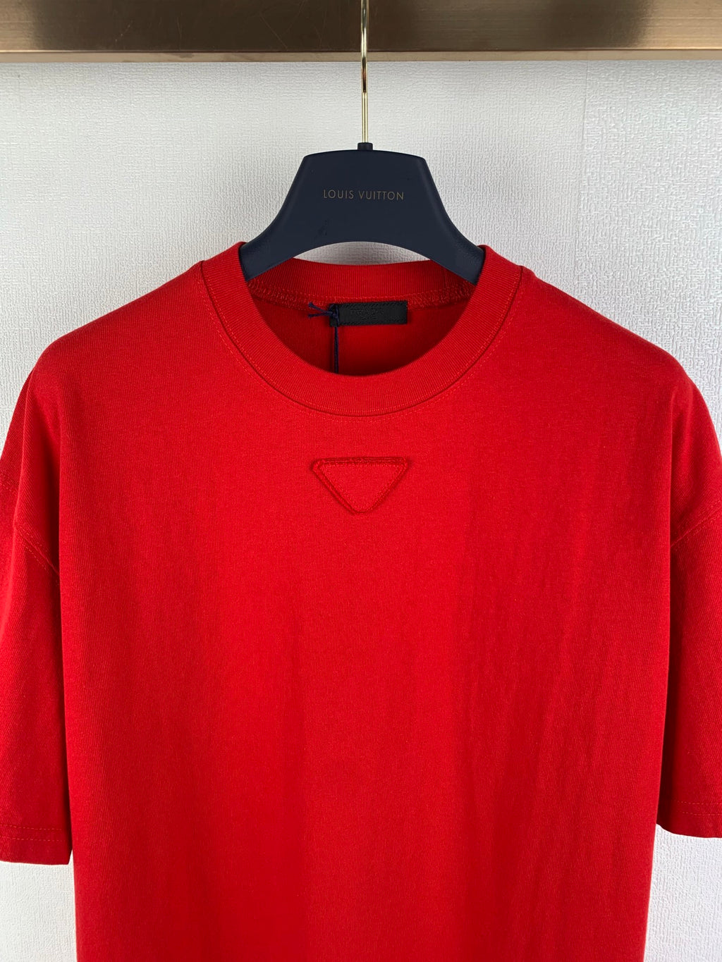 Red crew-neck T-shirt close-up, triangular chest logo, Louis Vuitton on hanger.
