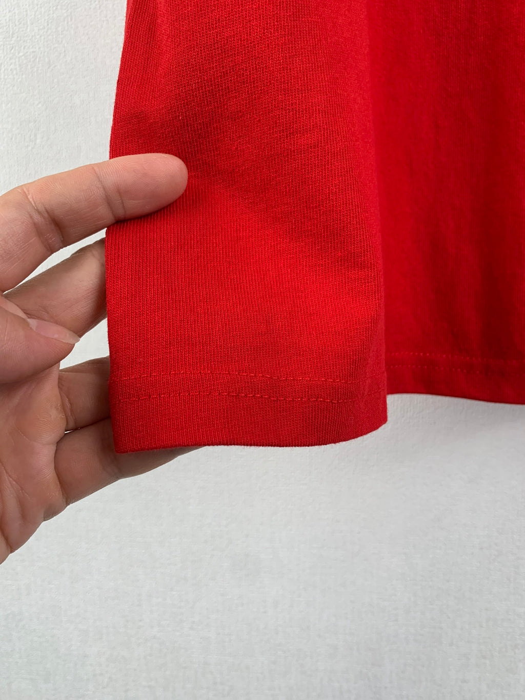 Red knit hem of short-sleeve T-shirt, hand showing cuff edge stitching.