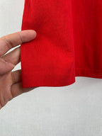 Red knit hem of short-sleeve T-shirt, hand showing cuff edge stitching.