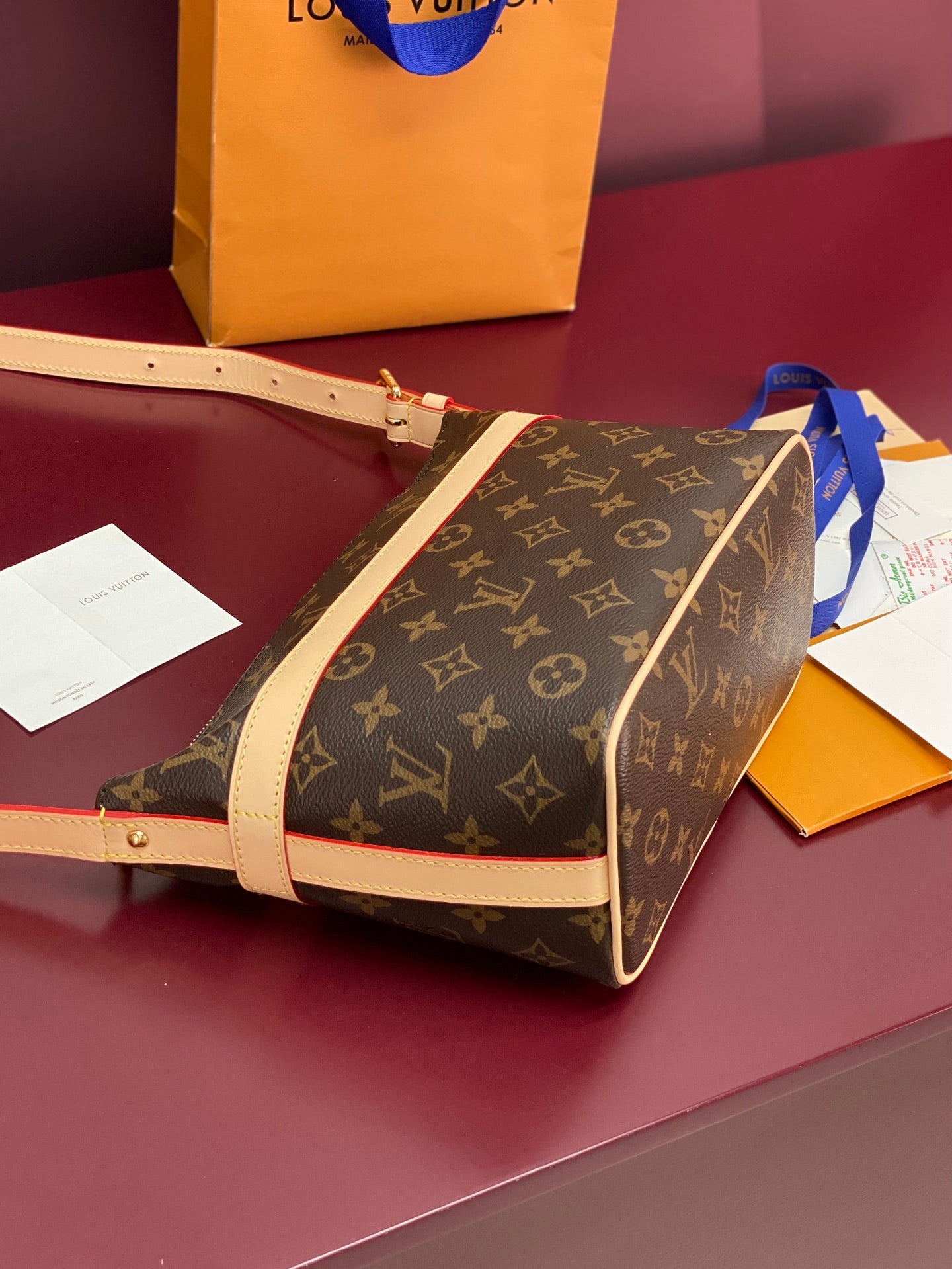 Louis Vuitton monogram bag with beige strap and zip top, shown at an angle