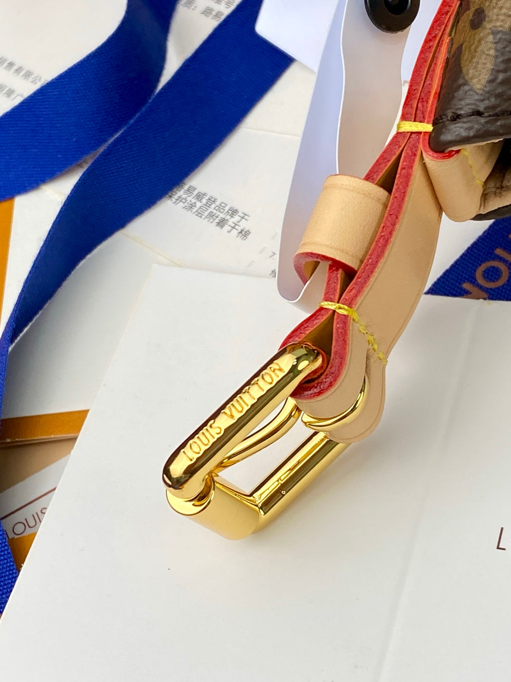 Louis Vuitton bag strap with gold clasp and cream tab, attached to monogram bag