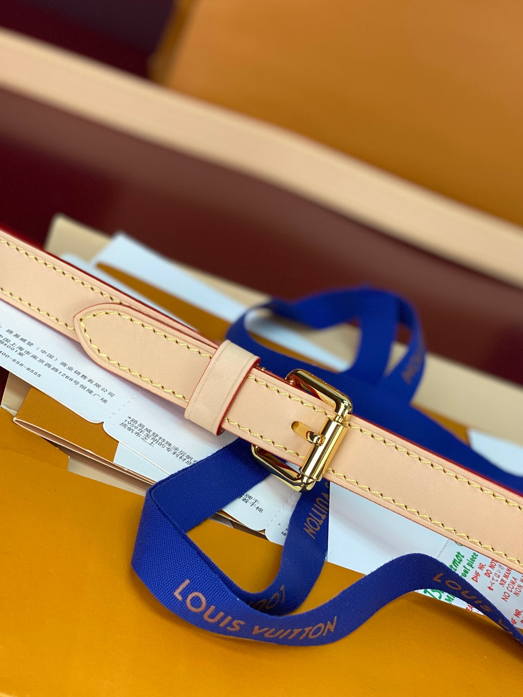 Louis Vuitton strap with gold buckle, tan edge stitching, and blue ribbon accessory