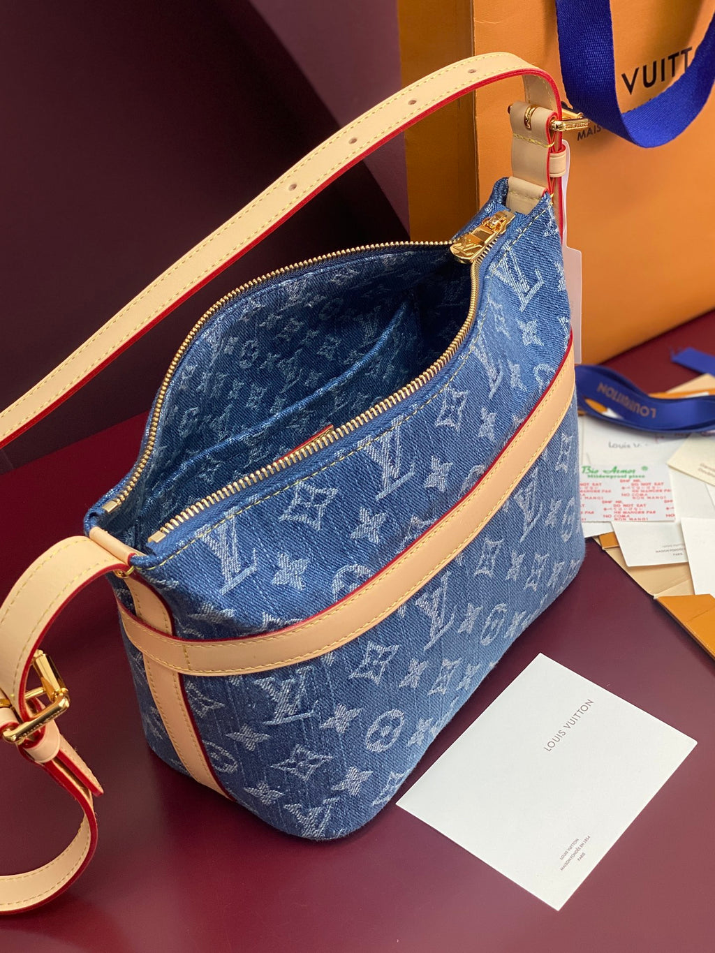 Louis Vuitton blue monogram bag with open zipper, tan strap, and gold zipper pull