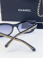 Black eyeglasses with gold chain detail across the temples and dark tinted lenses