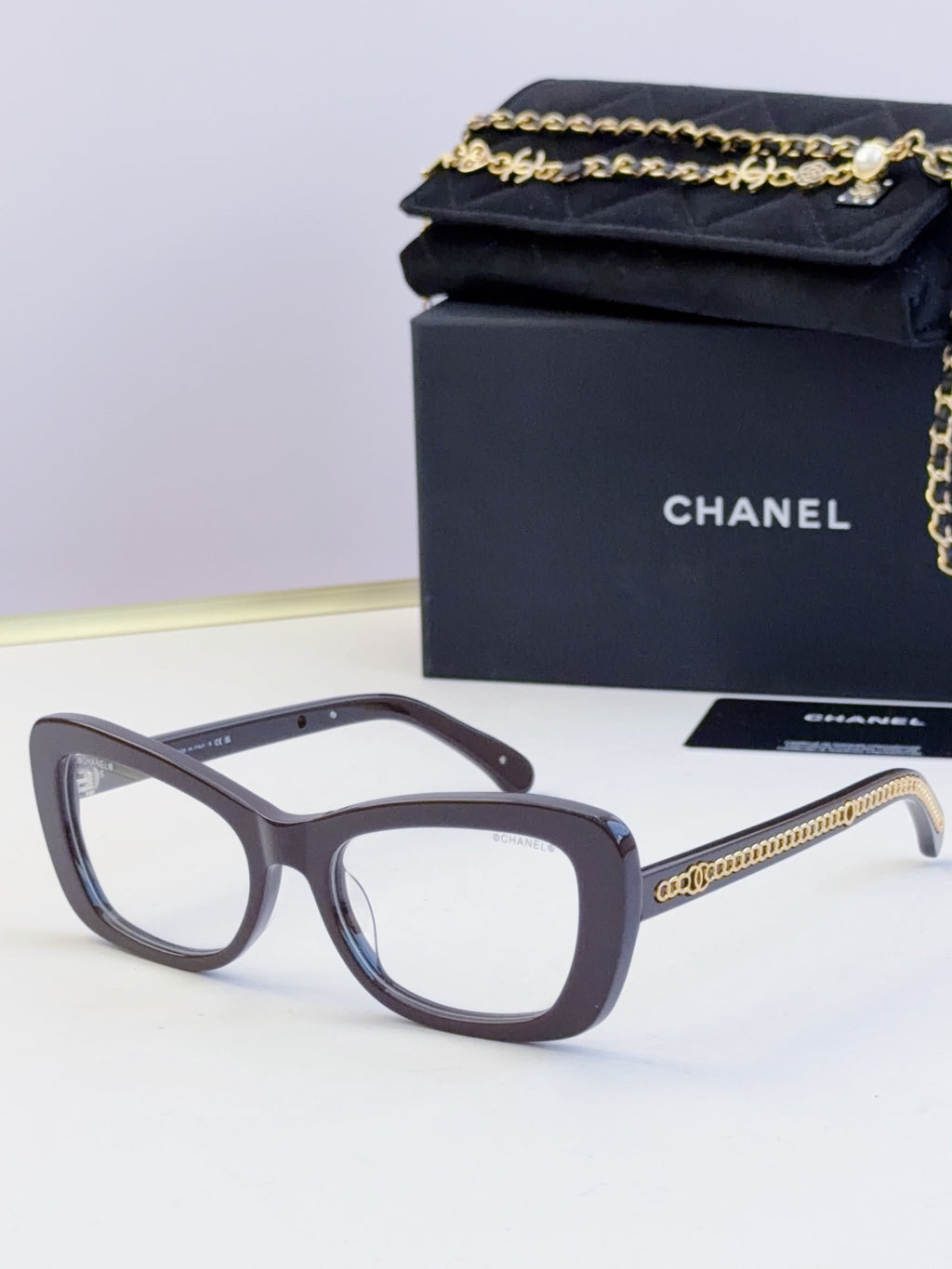 Gray glasses with oversized square frames, clear lenses, and gold chain on temples