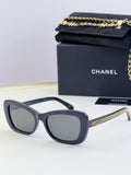 Dark glasses with oval frames, gray lenses, and gold chain detail on the temples
