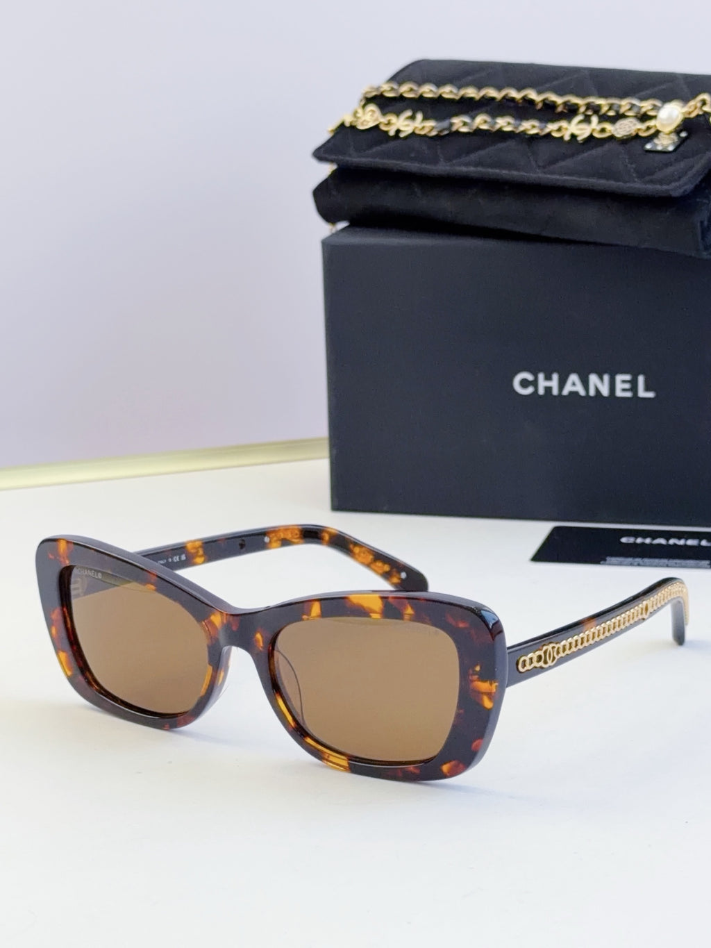 Tortoiseshell glasses with square frames, brown tinted lenses, and gold chain temples