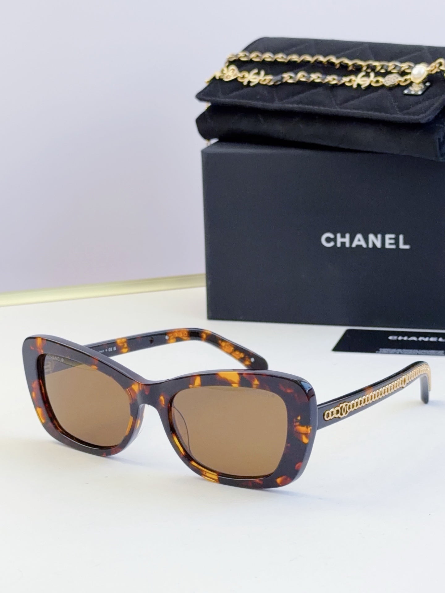 Tortoiseshell glasses with square frames, brown tinted lenses, and gold chain temples