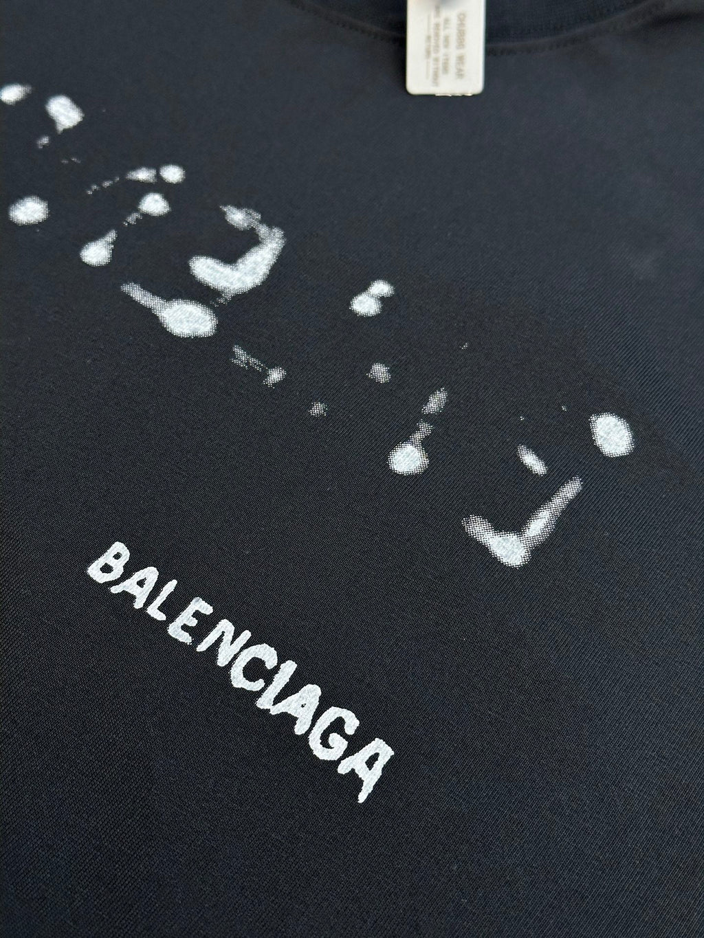 Balenciaga T-shirt fabric close-up with splatter print and BALENCIAGA text in white.
