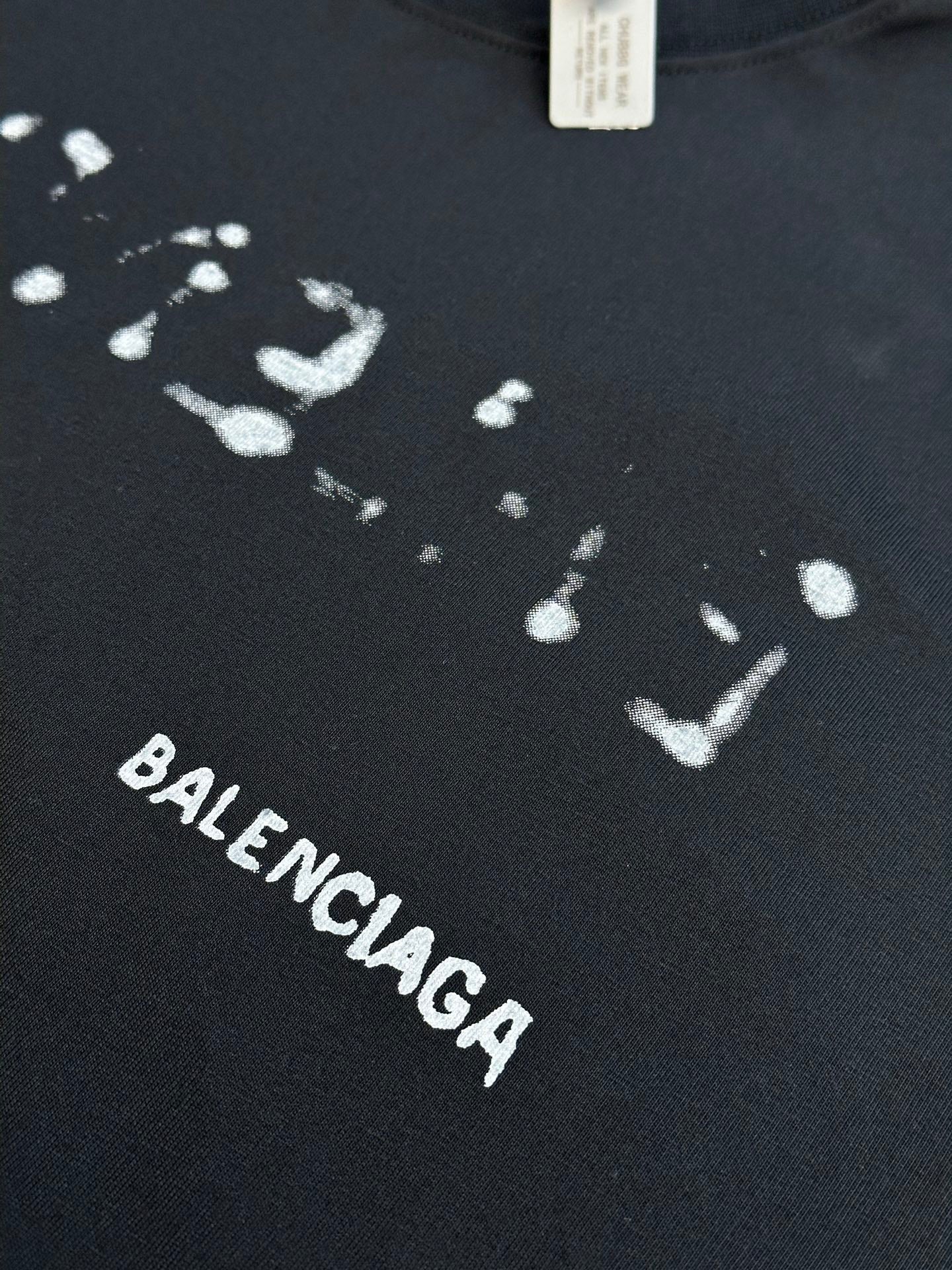 Balenciaga T-shirt fabric close-up with splatter print and BALENCIAGA text in white.