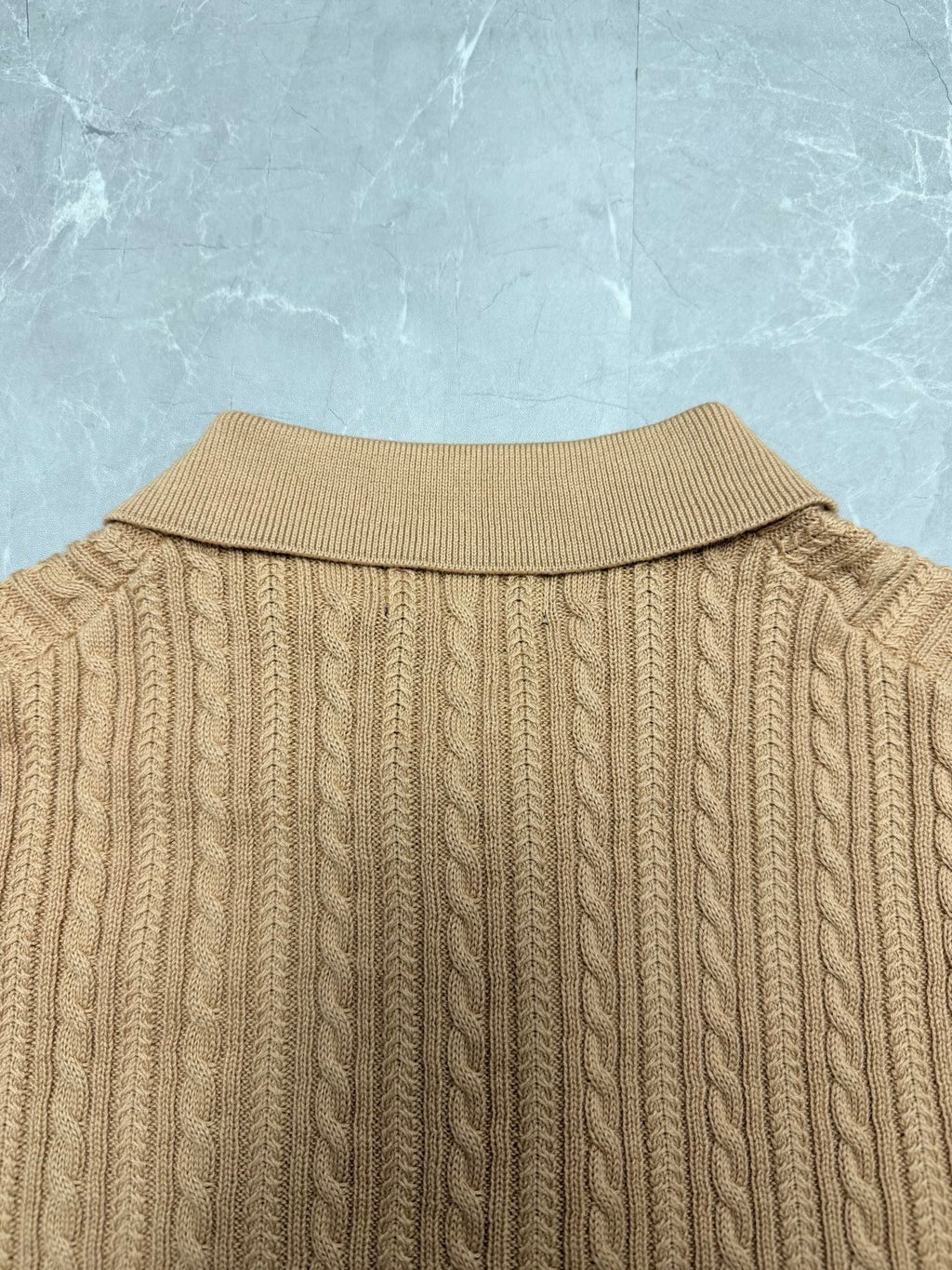 Beige knit polo shirt back with ribbed collar and vertical cable pattern.