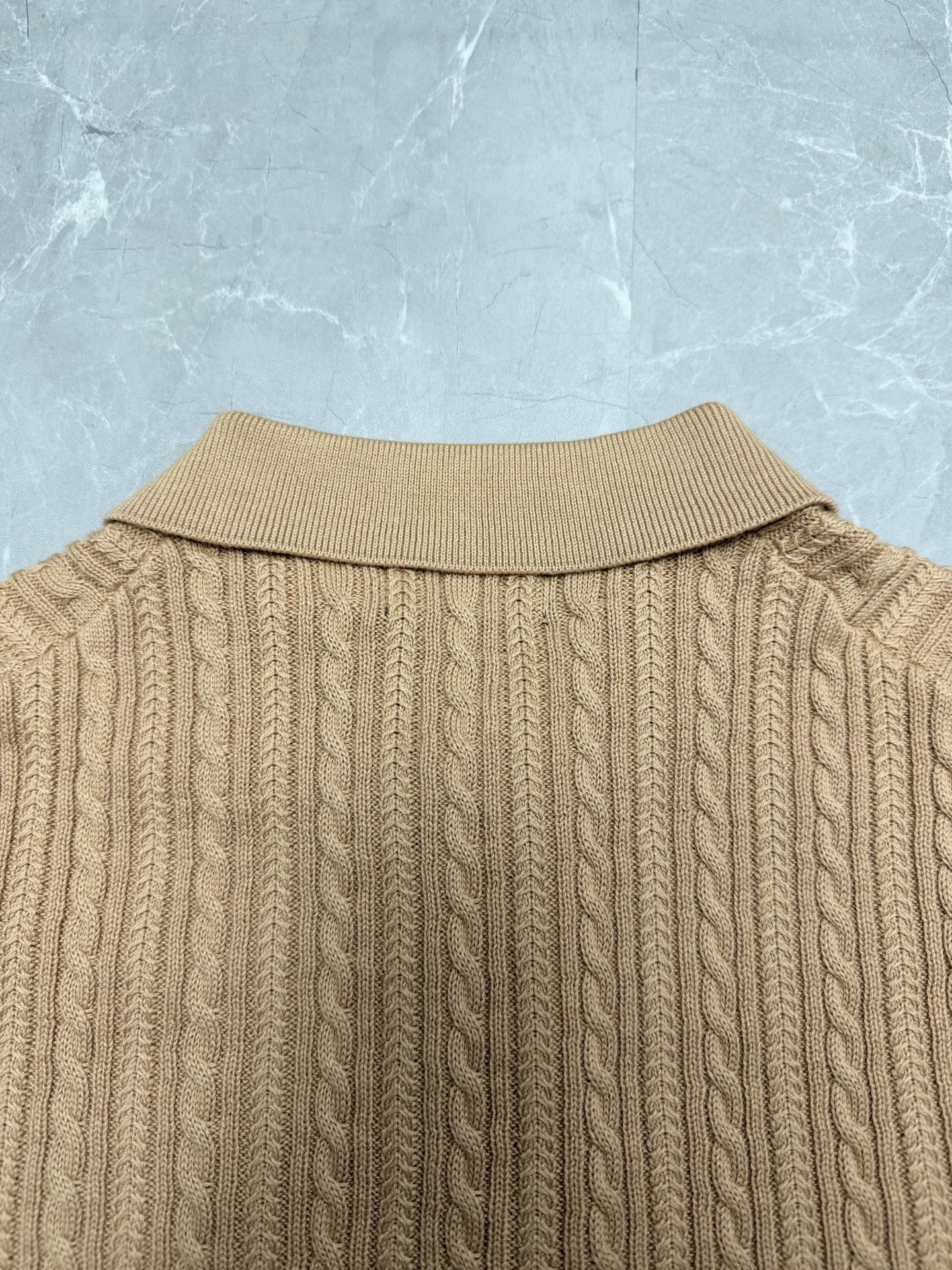 Beige knit polo shirt back with ribbed collar and vertical cable pattern.