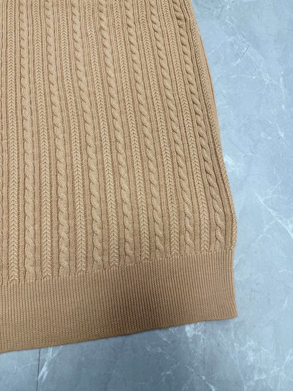 Beige knit polo shirt hem with vertical ribbed cable pattern.