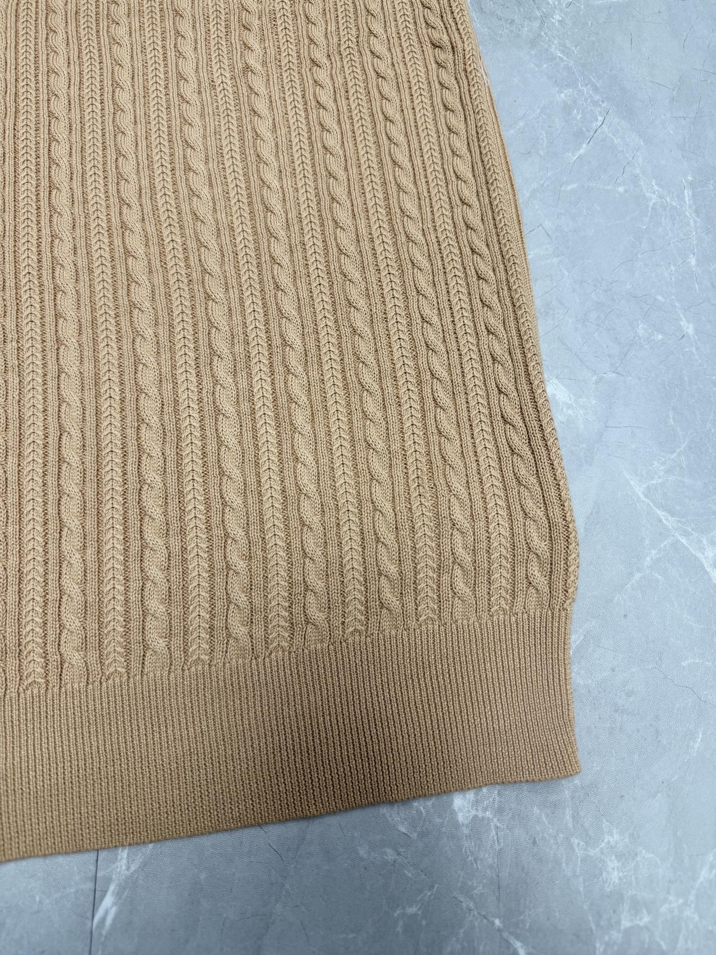 Beige knit polo shirt hem with vertical ribbed cable pattern.