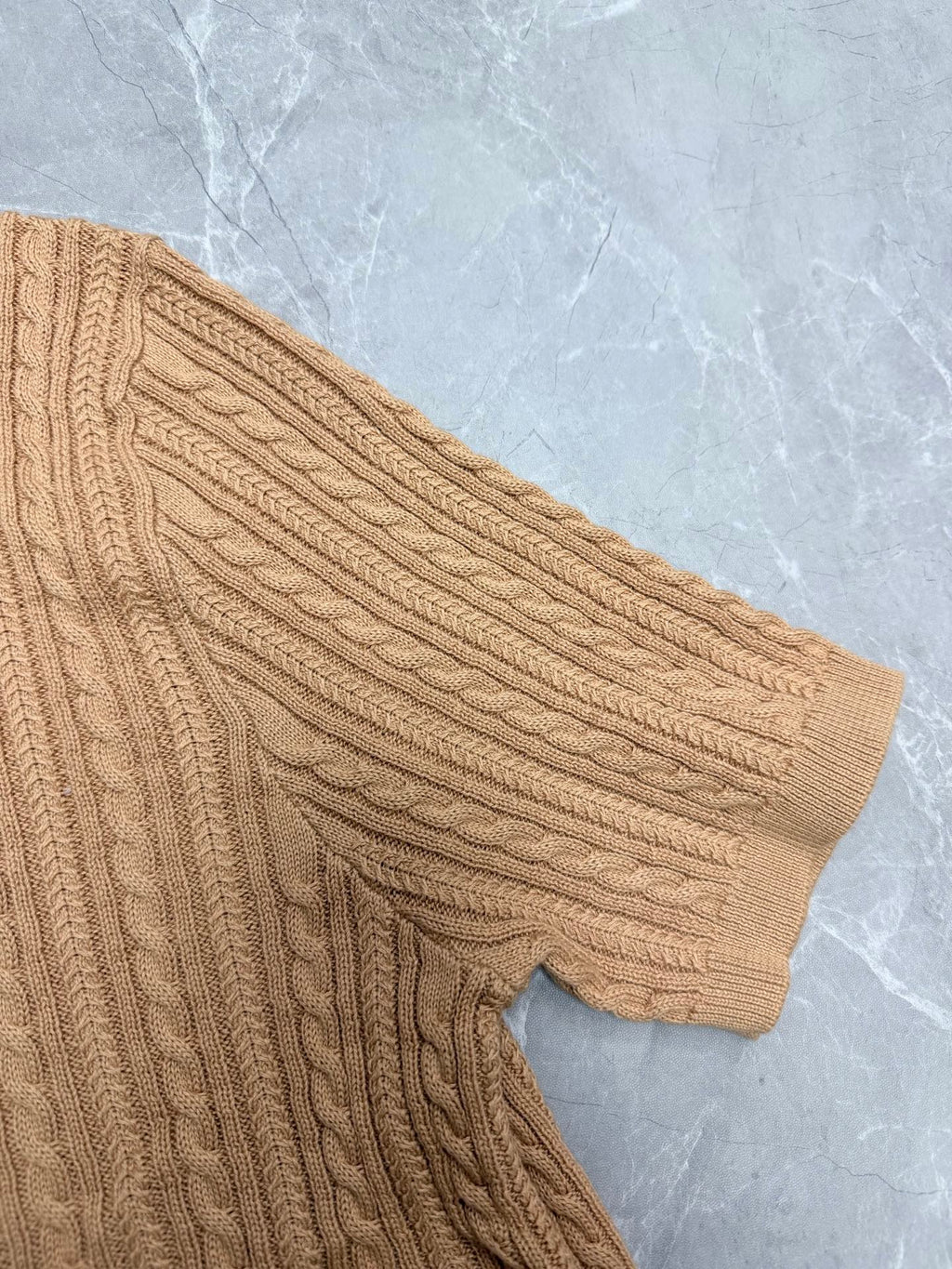 Beige cable-knit polo shirt sleeve with ribbed cuff.