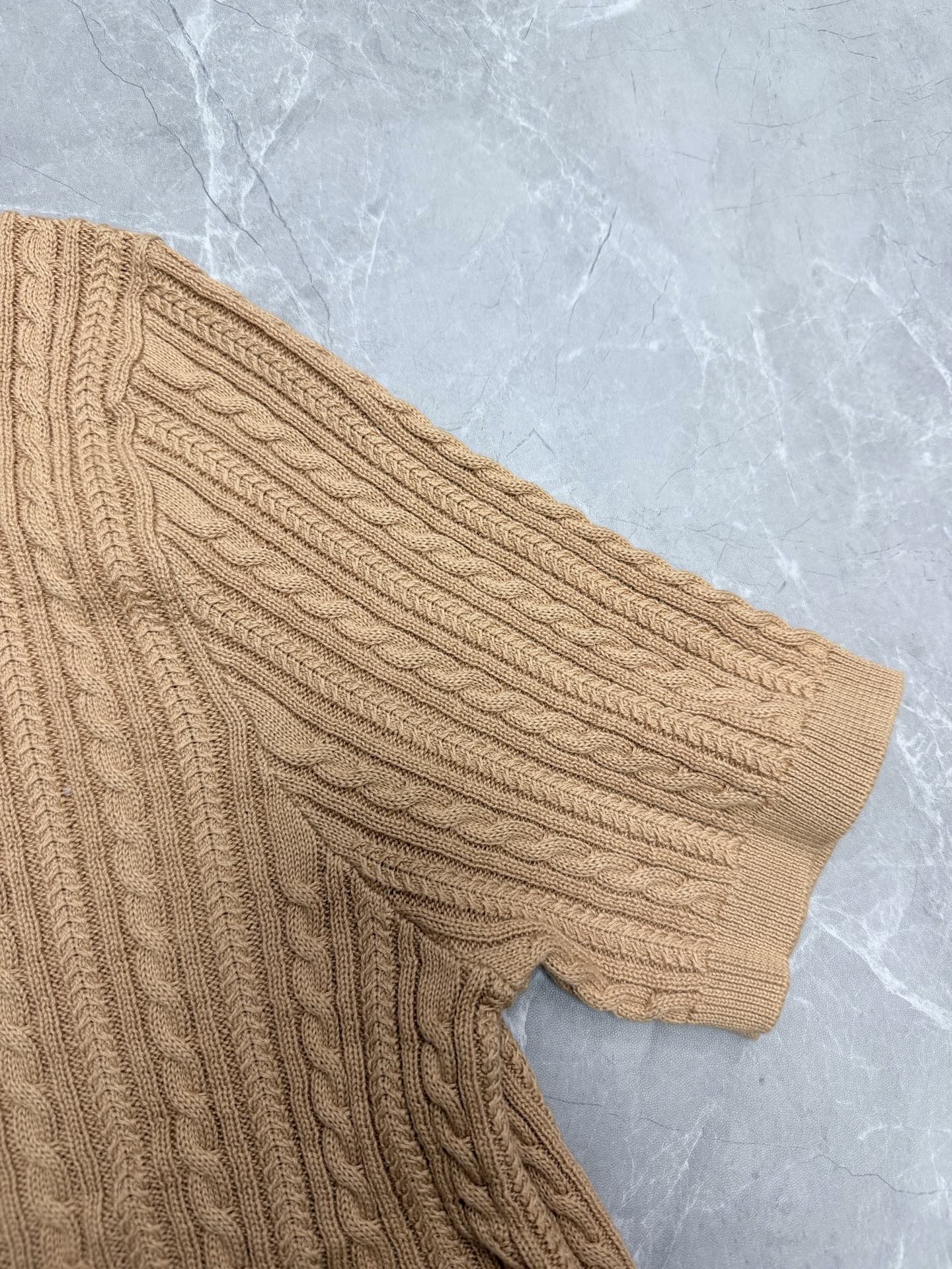 Beige cable-knit polo shirt sleeve with ribbed cuff.