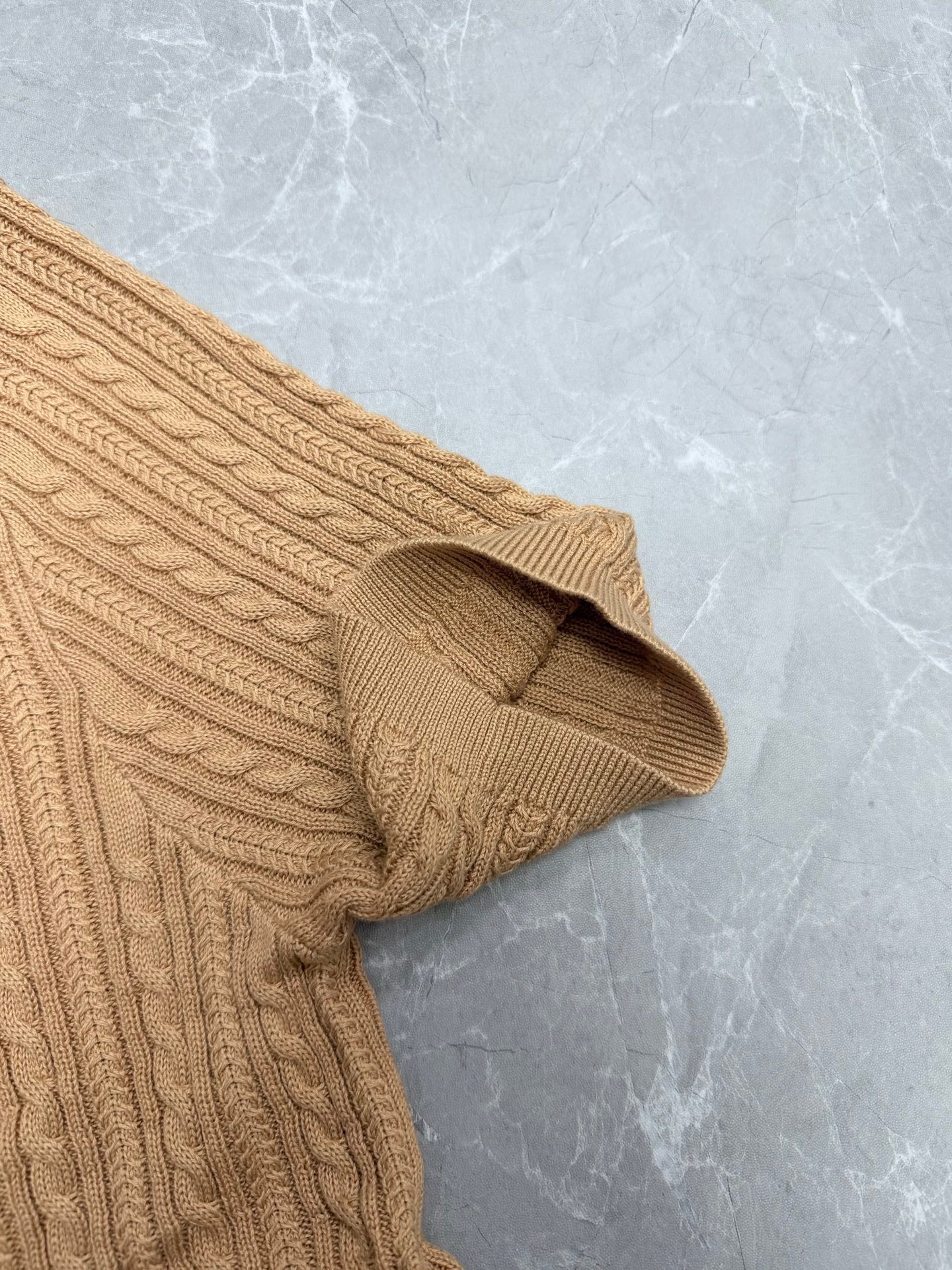 Beige cable-knit polo shirt sleeve cuff and shoulder seam detail.
