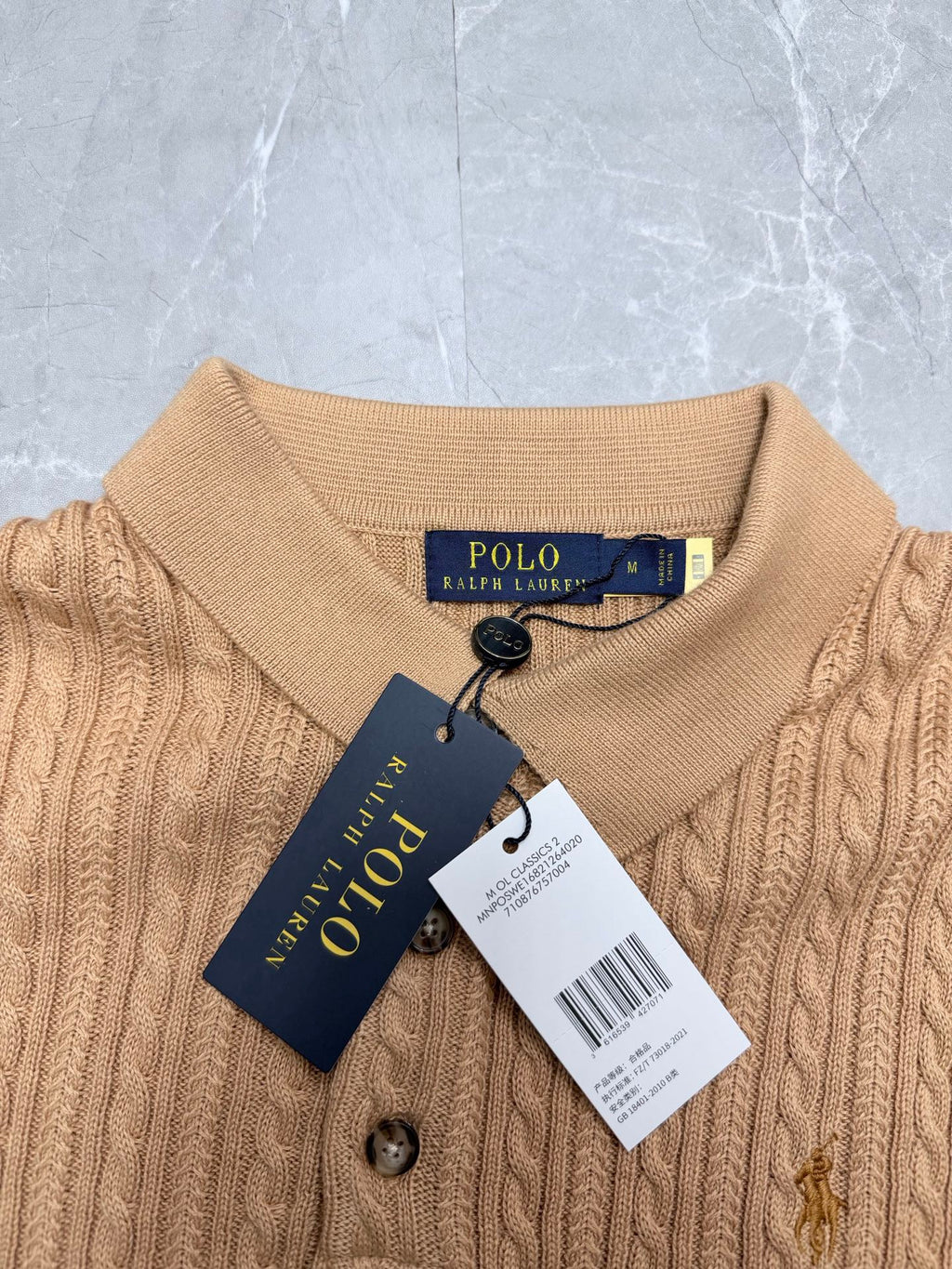 Beige knit polo shirt neckline with button placket and attached Polo Ralph Lauren tag.