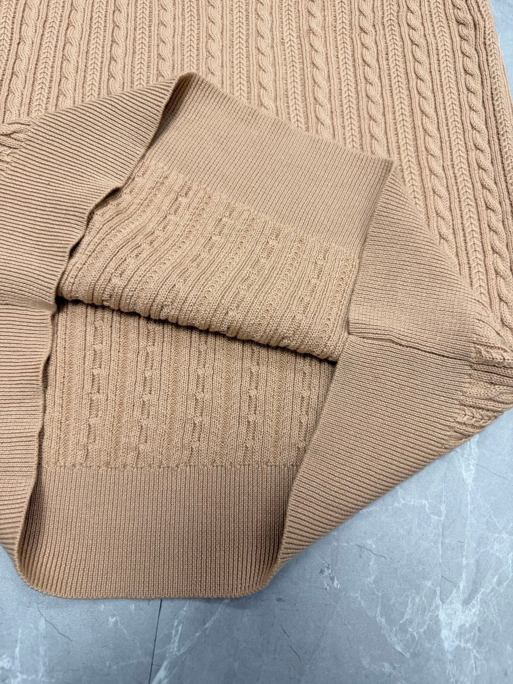 Beige knit polo shirt hem panel with ribbed trim and cable knit detailing.
