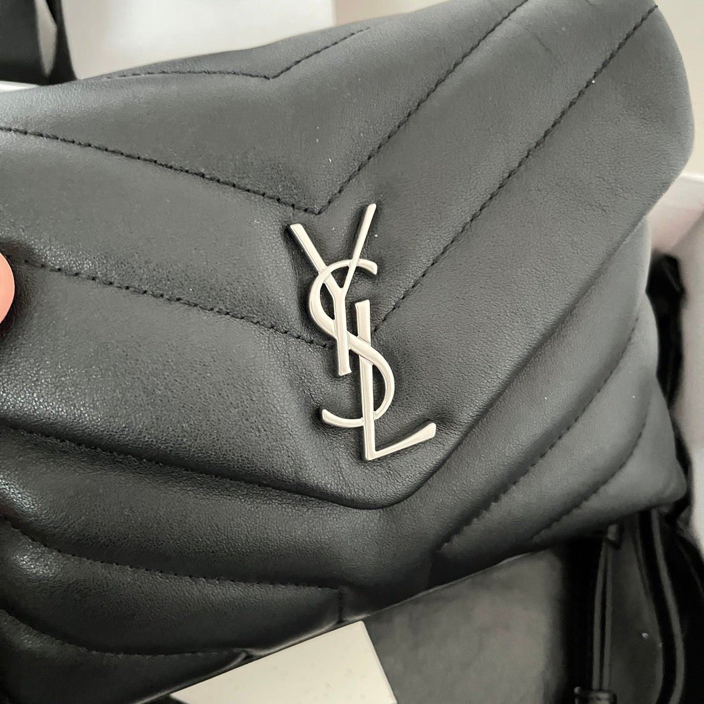 YSL bag close-up of YSL logo on dark quilted leather flap