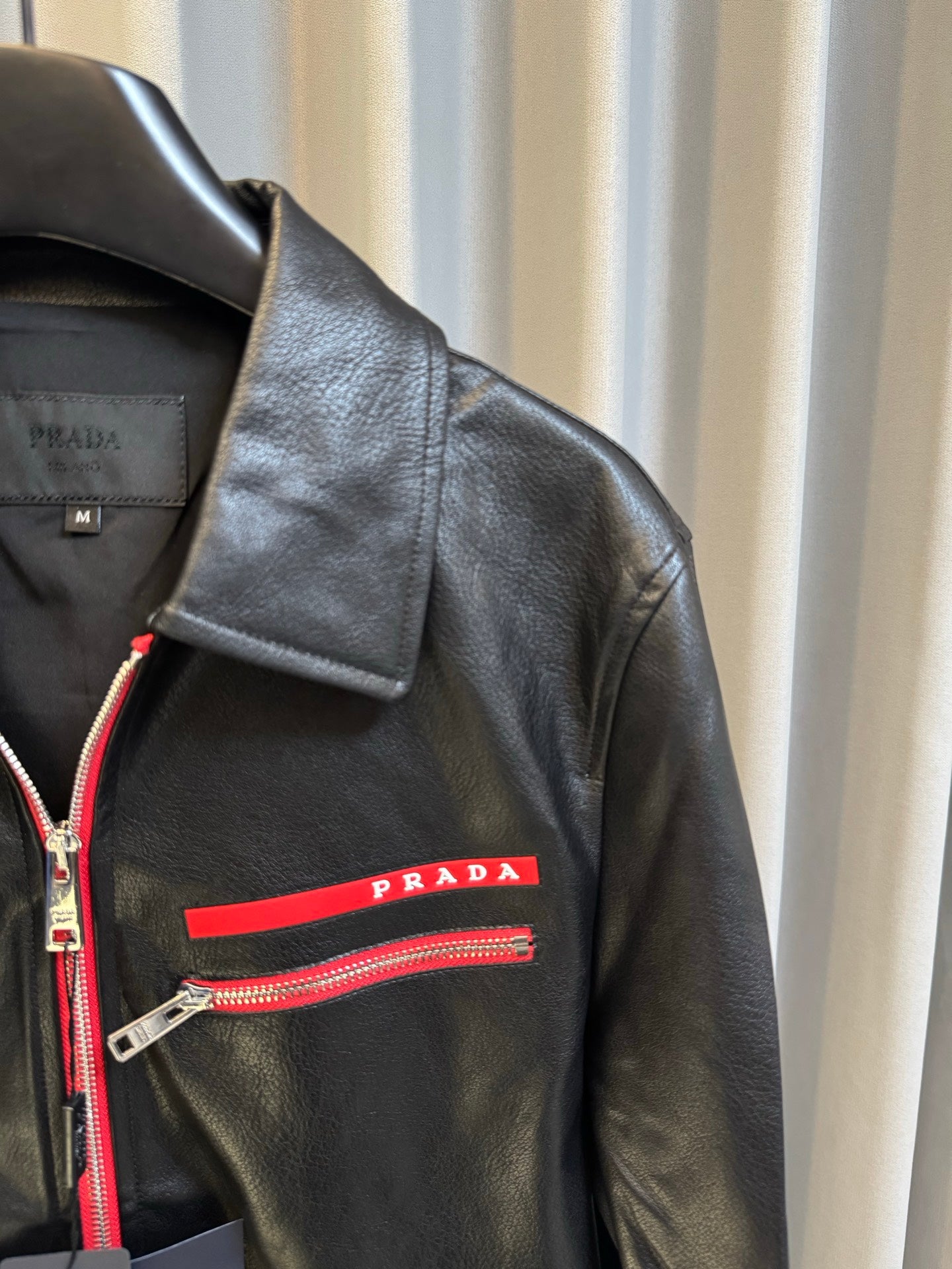 Shoulder and chest detail of Prada black leather jacket with red logo stripe