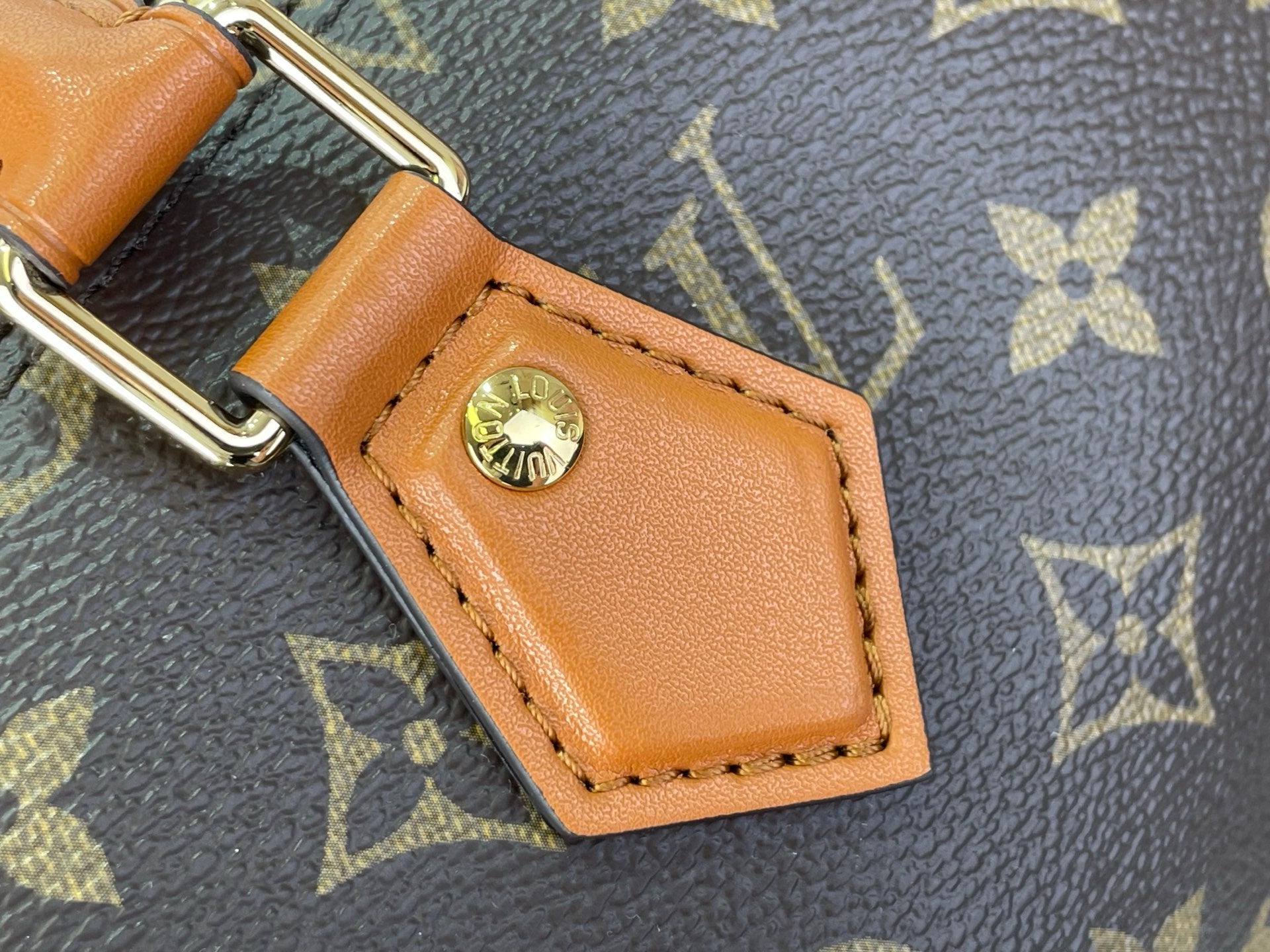 Tan leather strap patch with gold-tone rivet buckle on monogram canvas