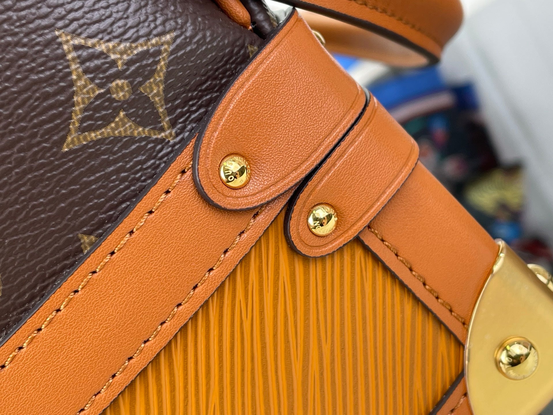 Tan leather strap attachment with gold-tone snap button on monogram canvas