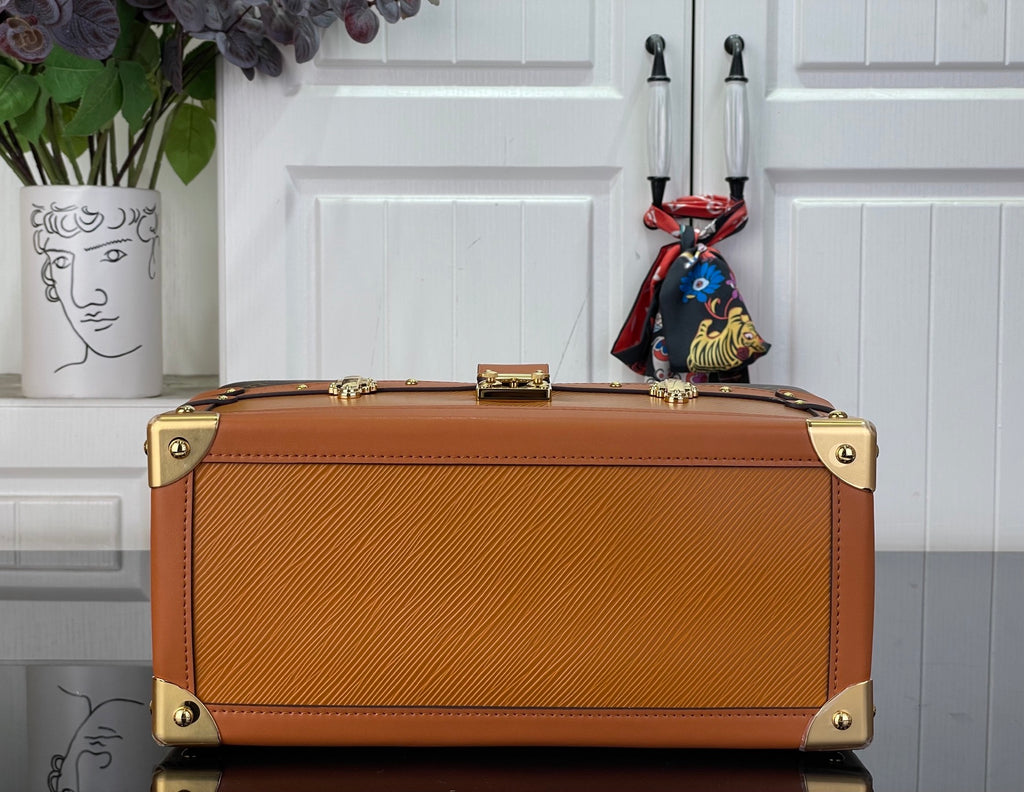 Monogram handbag with tan leather top, gold-tone corner feet, and front metal plates