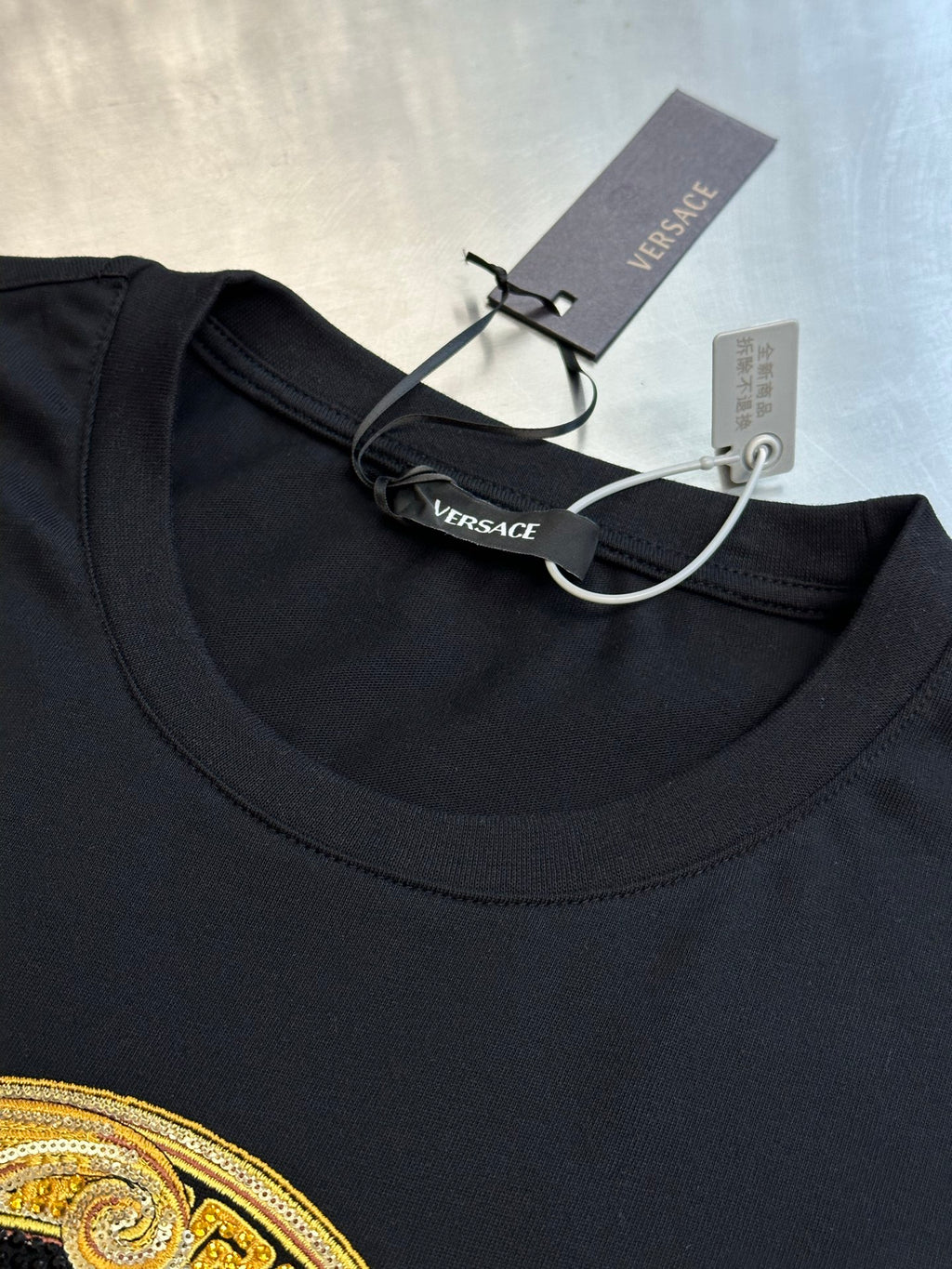 Versace black T-shirt neckline with logo tag and paper price tag
