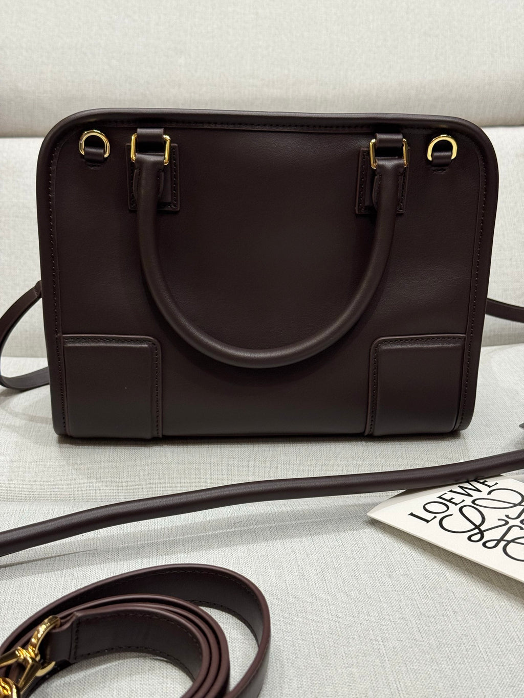 Dark brown leather structured bag with top handles, gold zipper, and side tabs