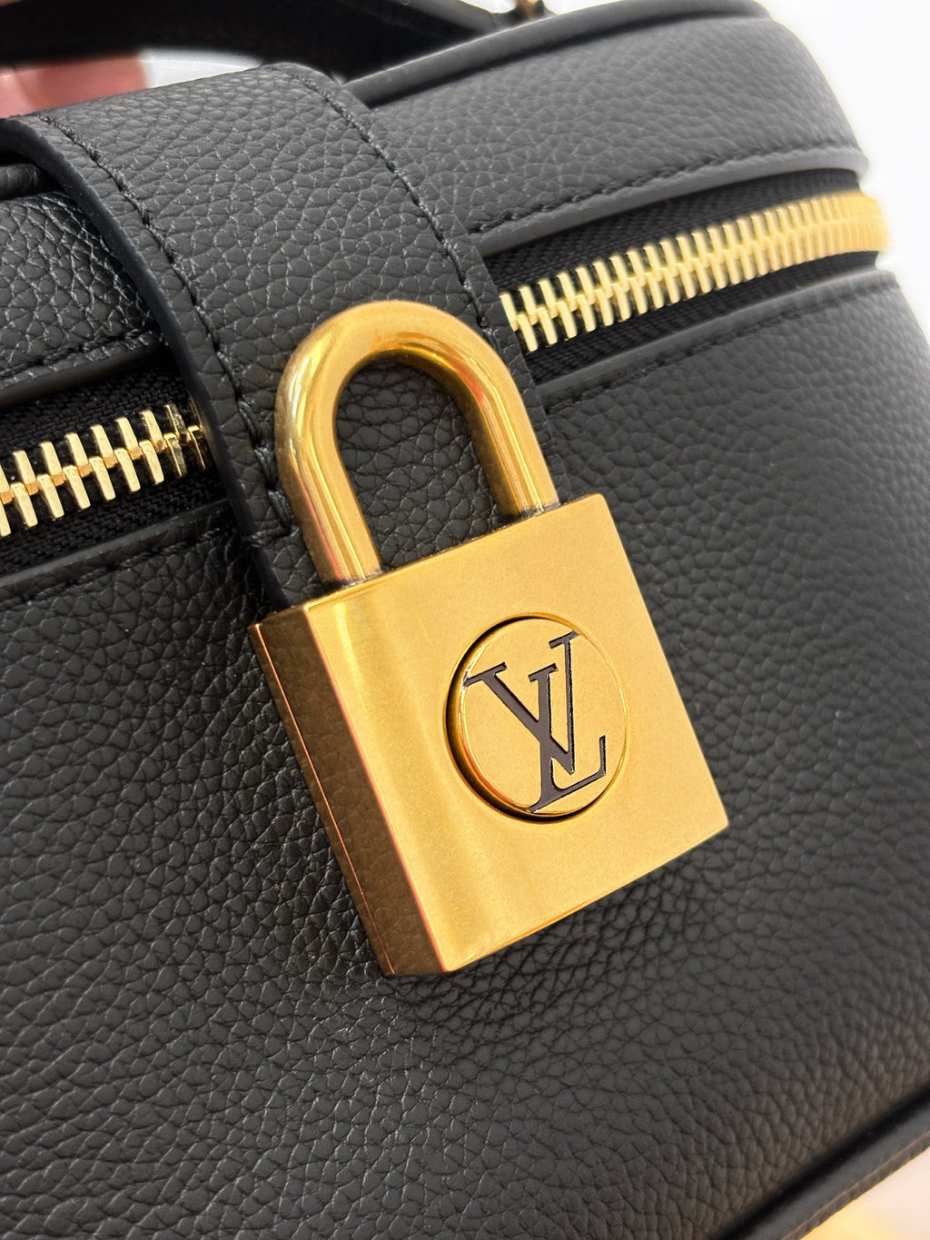 Louis Vuitton padlock hardware close-up in gold on dark black textured leather