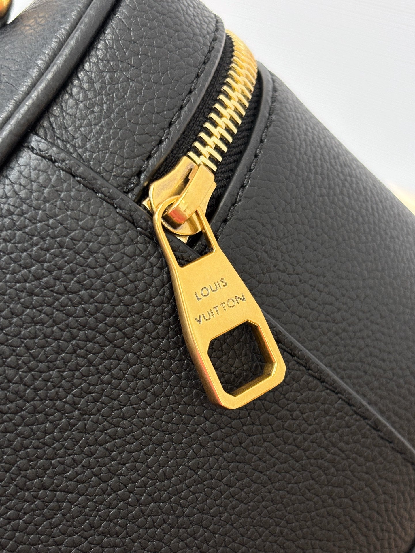 Louis Vuitton gold zipper pull close-up on dark black pebbled leather