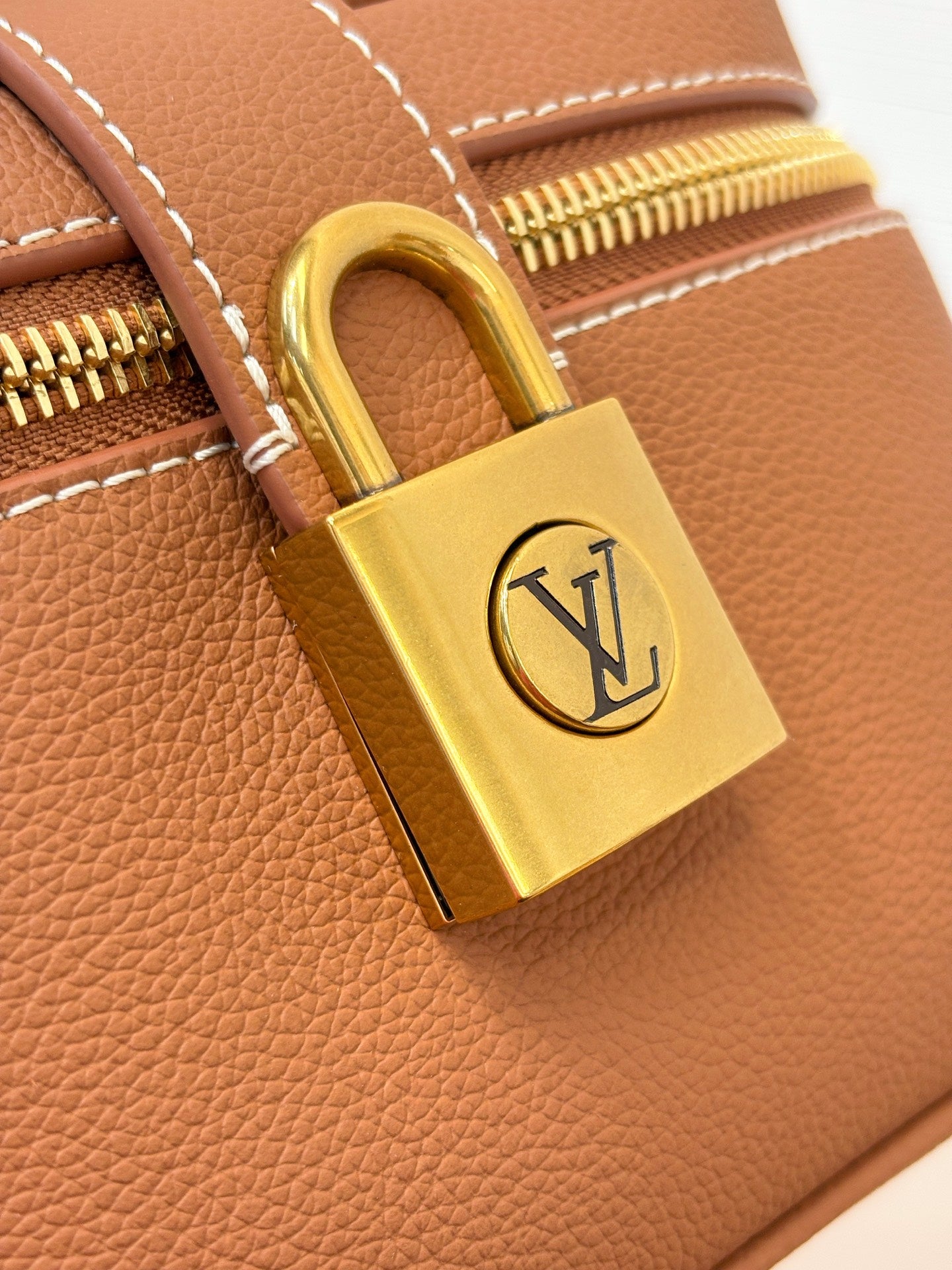 Louis Vuitton brown leather bag padlock with gold clasp and LV logo, close-up