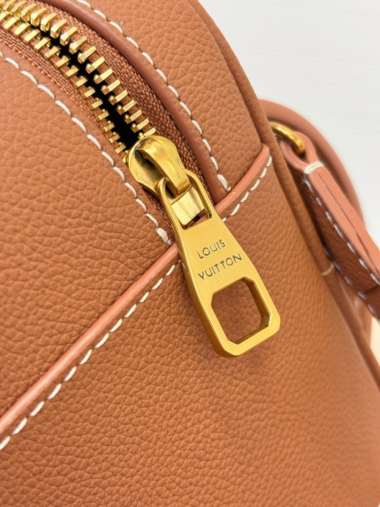 Louis Vuitton brown leather bag zipper pull with gold hardware and LV logo, close-up