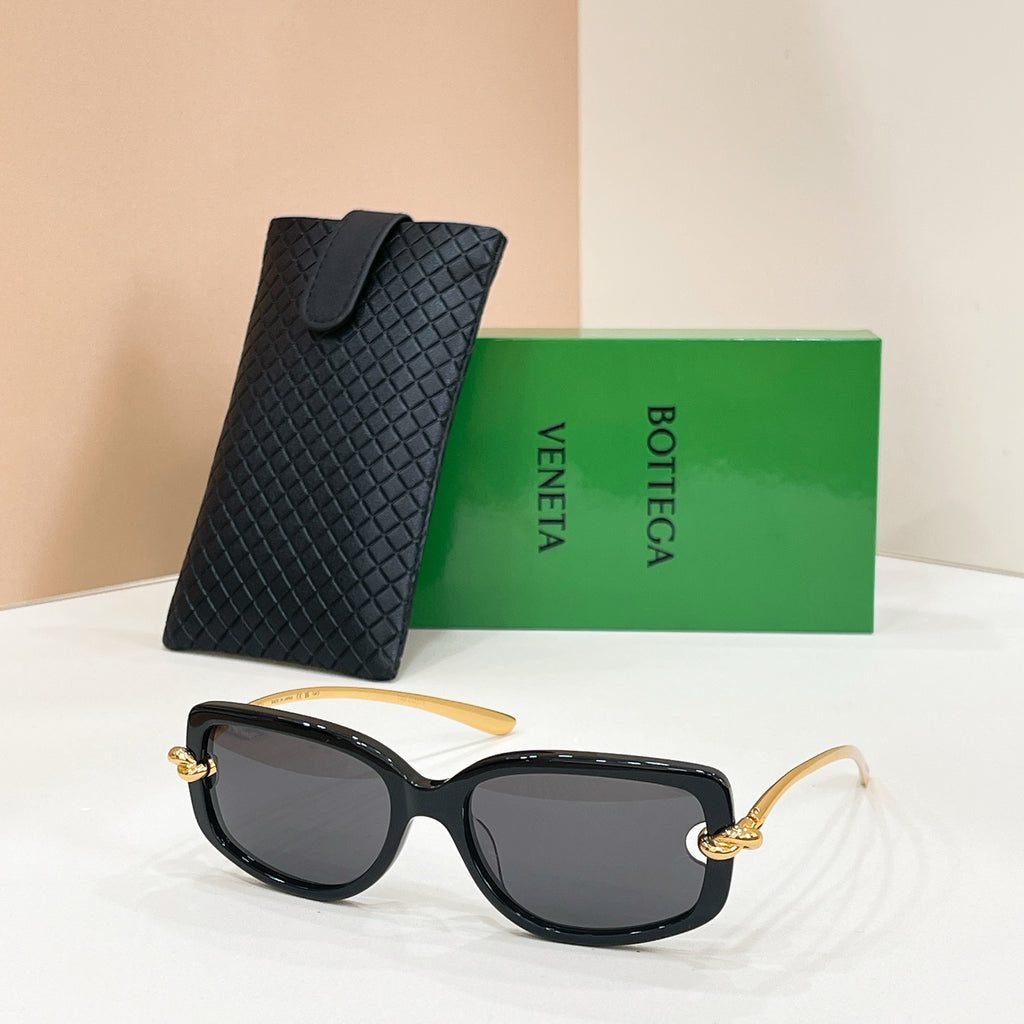 Black sunglasses with dark lenses and gold-tone accents, with a black case