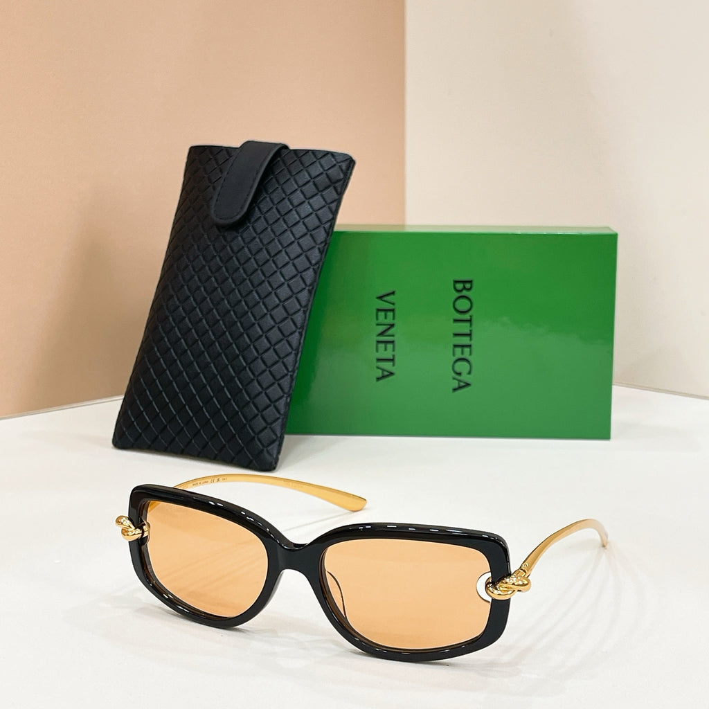 Black sunglasses with amber lenses and gold-tone accents, paired with a black case