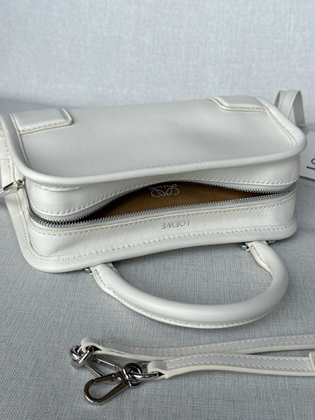 White leather handbag with top zipper, brown lining, and crossbody strap