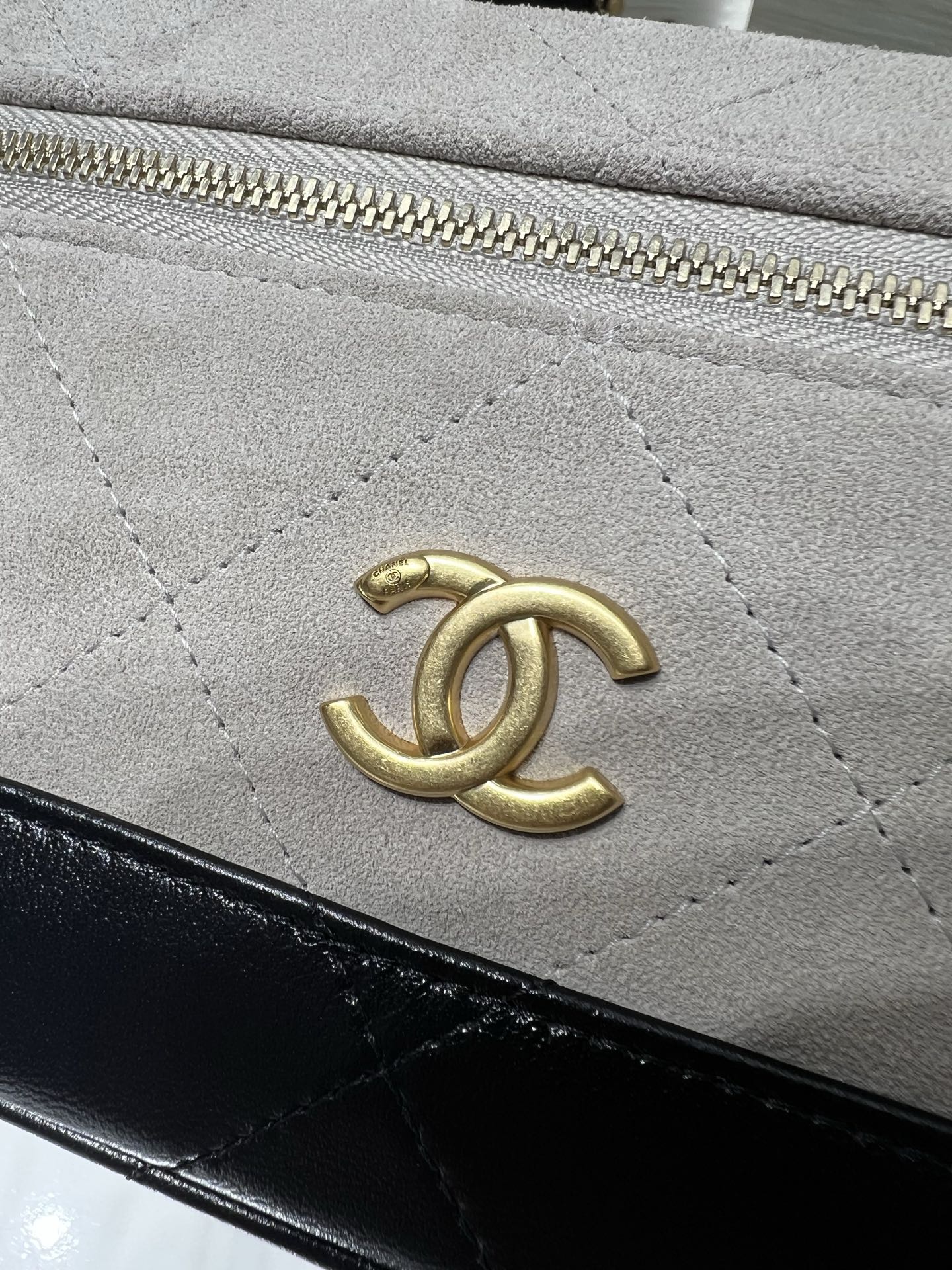 Chanel bag close-up of gold logo on light gray quilted leather with black trim