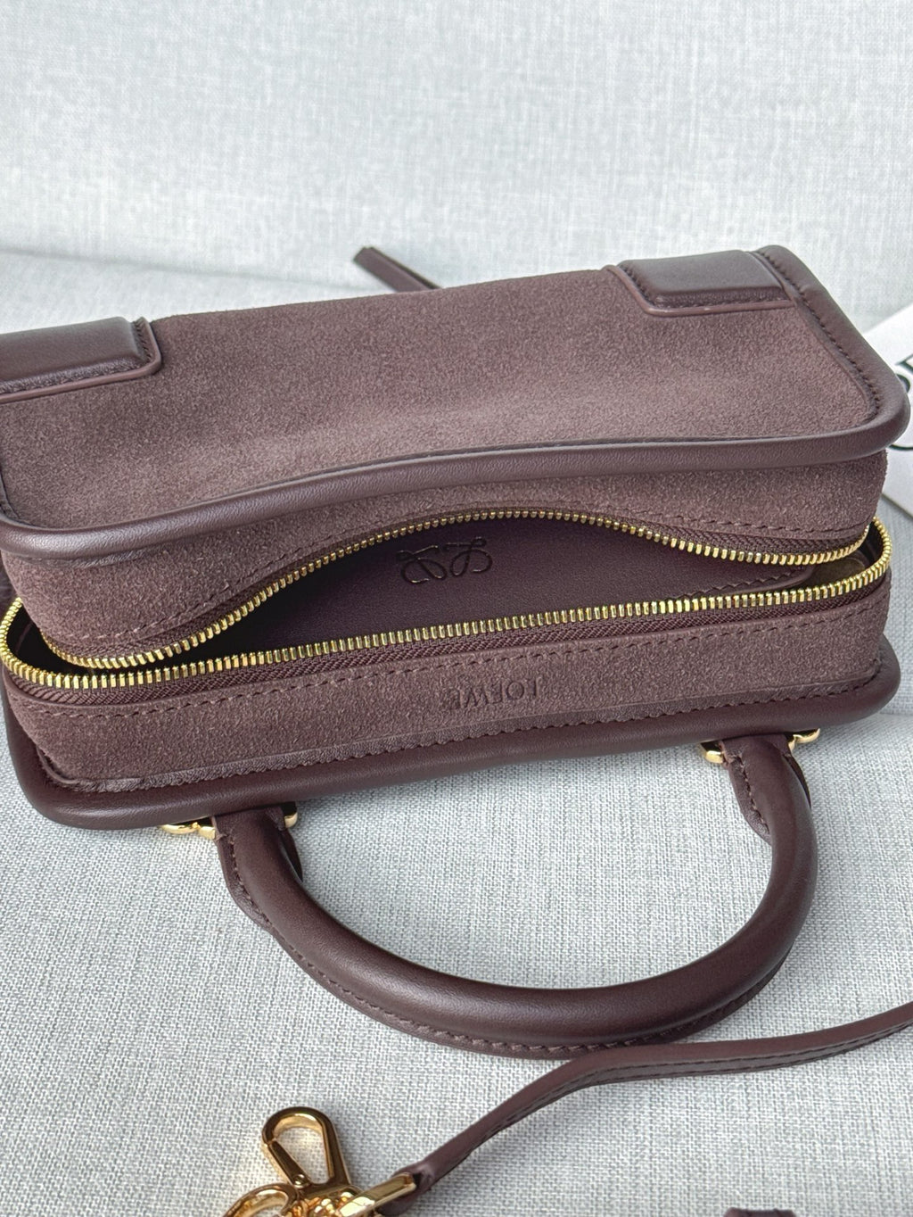 Loewe bag with top zipper and curved strap, textured exterior with gold trim.
