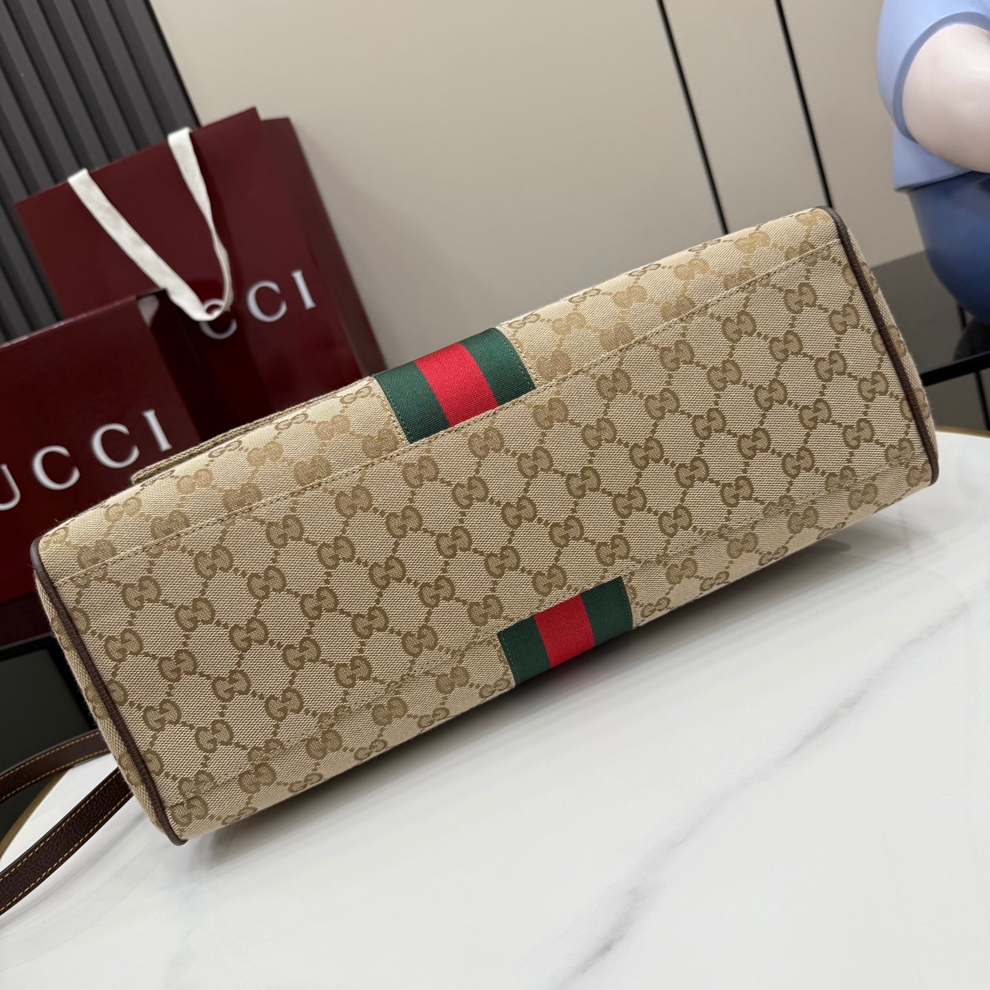 GG-print clutch-style bag with green and red stripe and brown leather trim, angled view