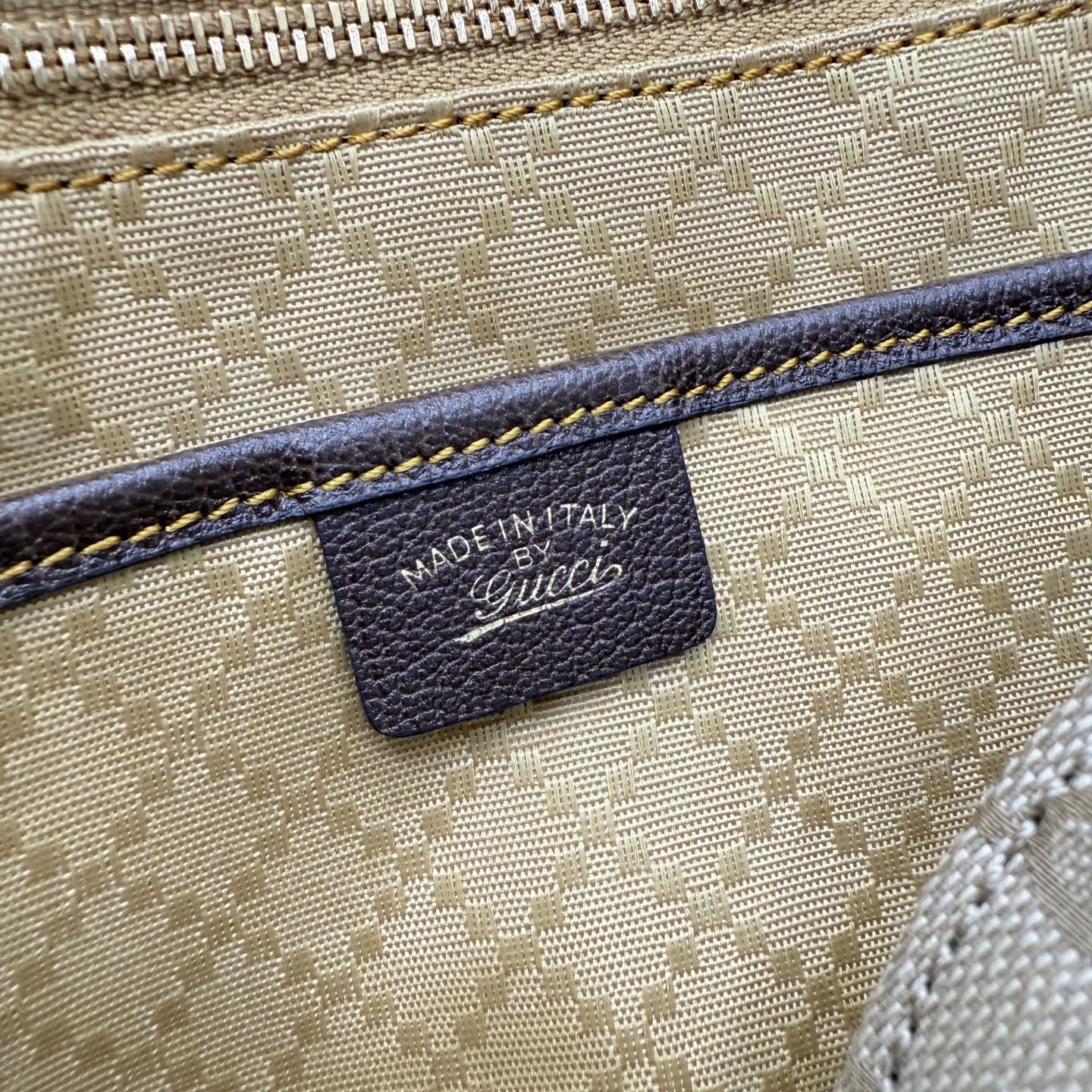 Fabric bag detail with blue trim stitching and leather brand patch reading "Gucci"