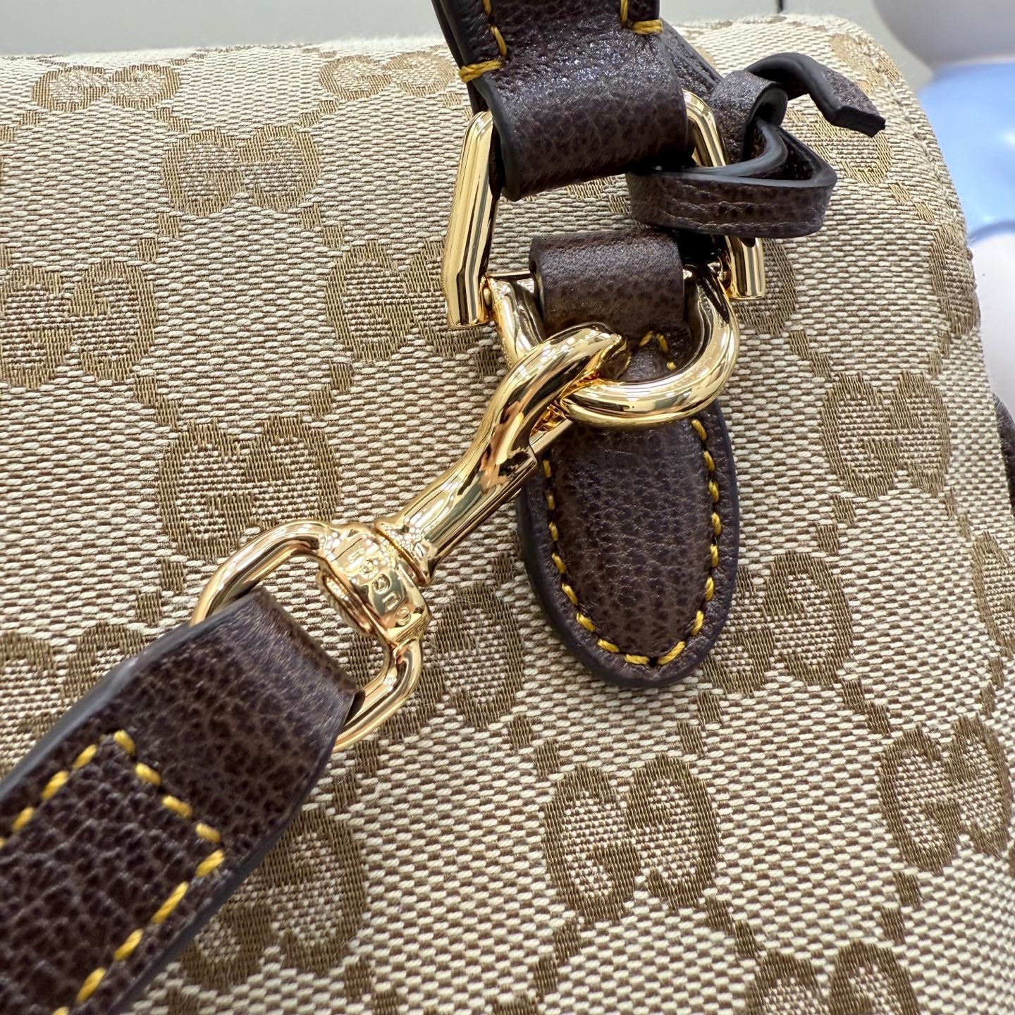 GG-print bag hardware close-up with gold-tone rings and brown leather strap attachment